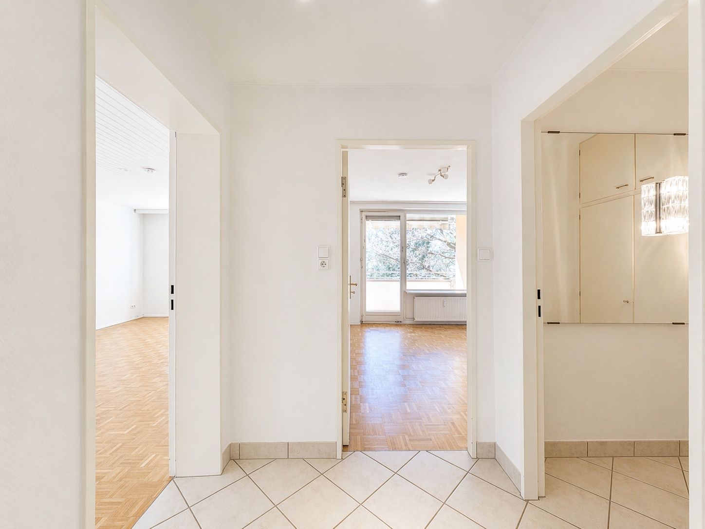 Heller Flur mit Fliesenboden, Türen zu zwei Zimmern und Fenster im Hintergrund.