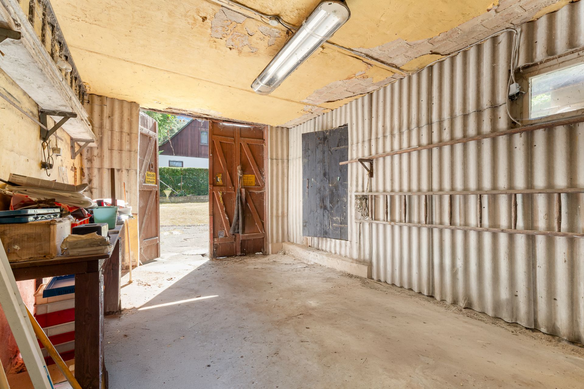 Innenansicht einer leeren Garage mit Wellblechwänden und geöffneten Holztoren.