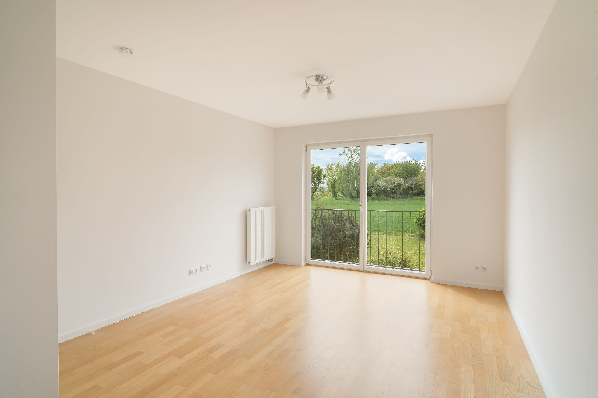 Helles, leeres Zimmer mit Parkettboden und großer Glas-Schiebetür zum Garten.