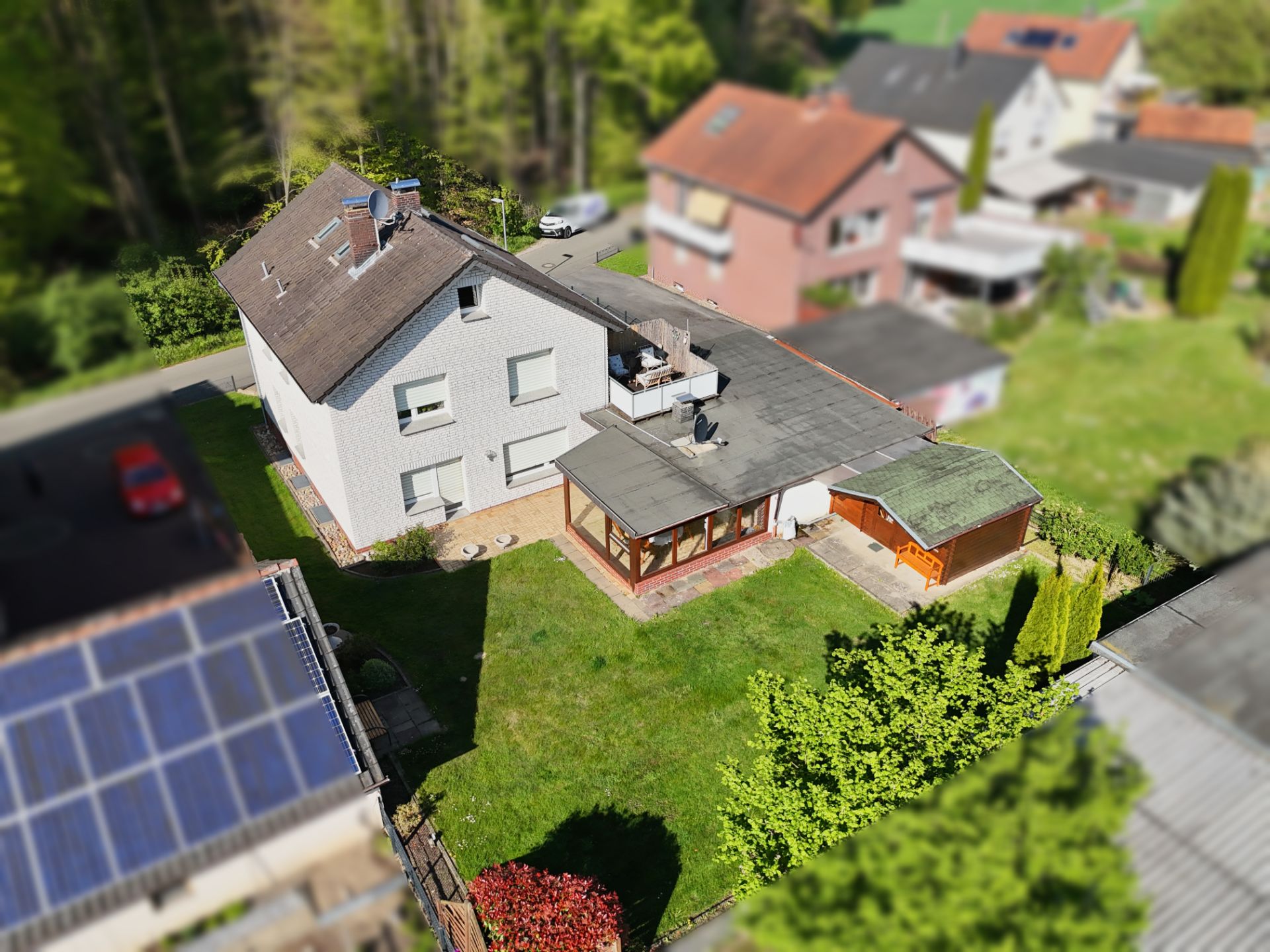 Luftaufnahme eines Einfamilienhauses mit Wintergarten und großem Garten.