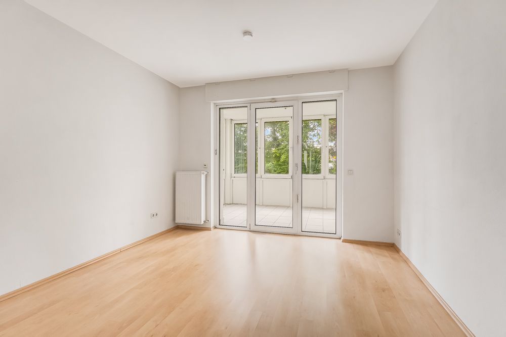 Leerer Raum mit hellem Holzboden und Glas-Doppeltür zu einem Balkon.