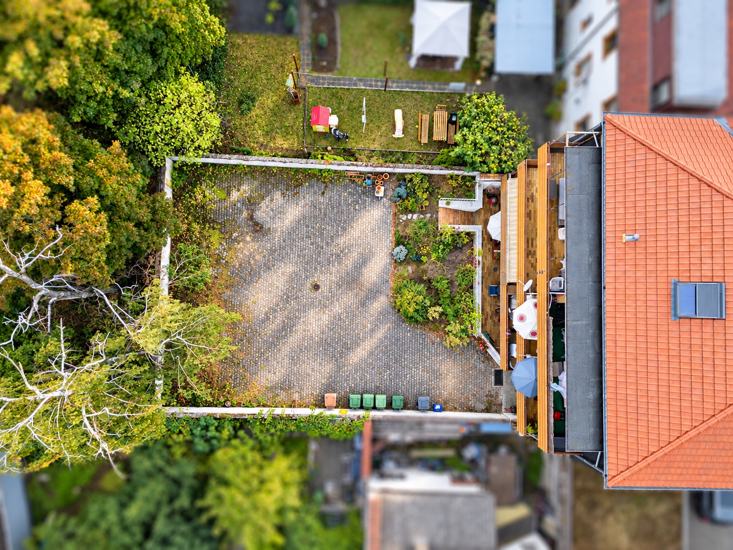 Luftaufnahme von Hof und Garten eines Wohnhauses mit Pflanzen, Terrasse und Mülltonnen.