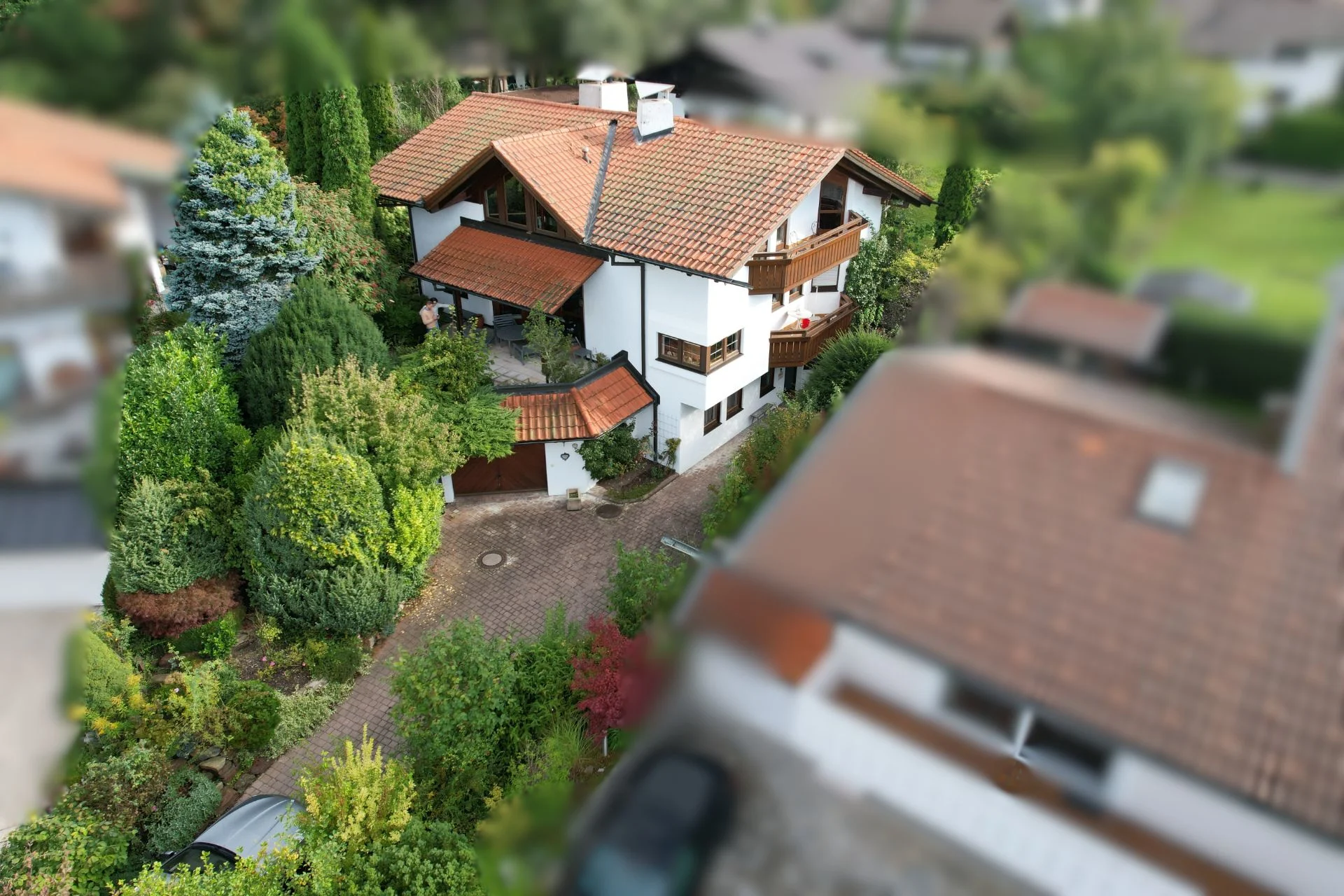 Großes weißes Wohnhaus mit roten Dachziegeln, umgeben von viel Grün und einer Einfahrt.