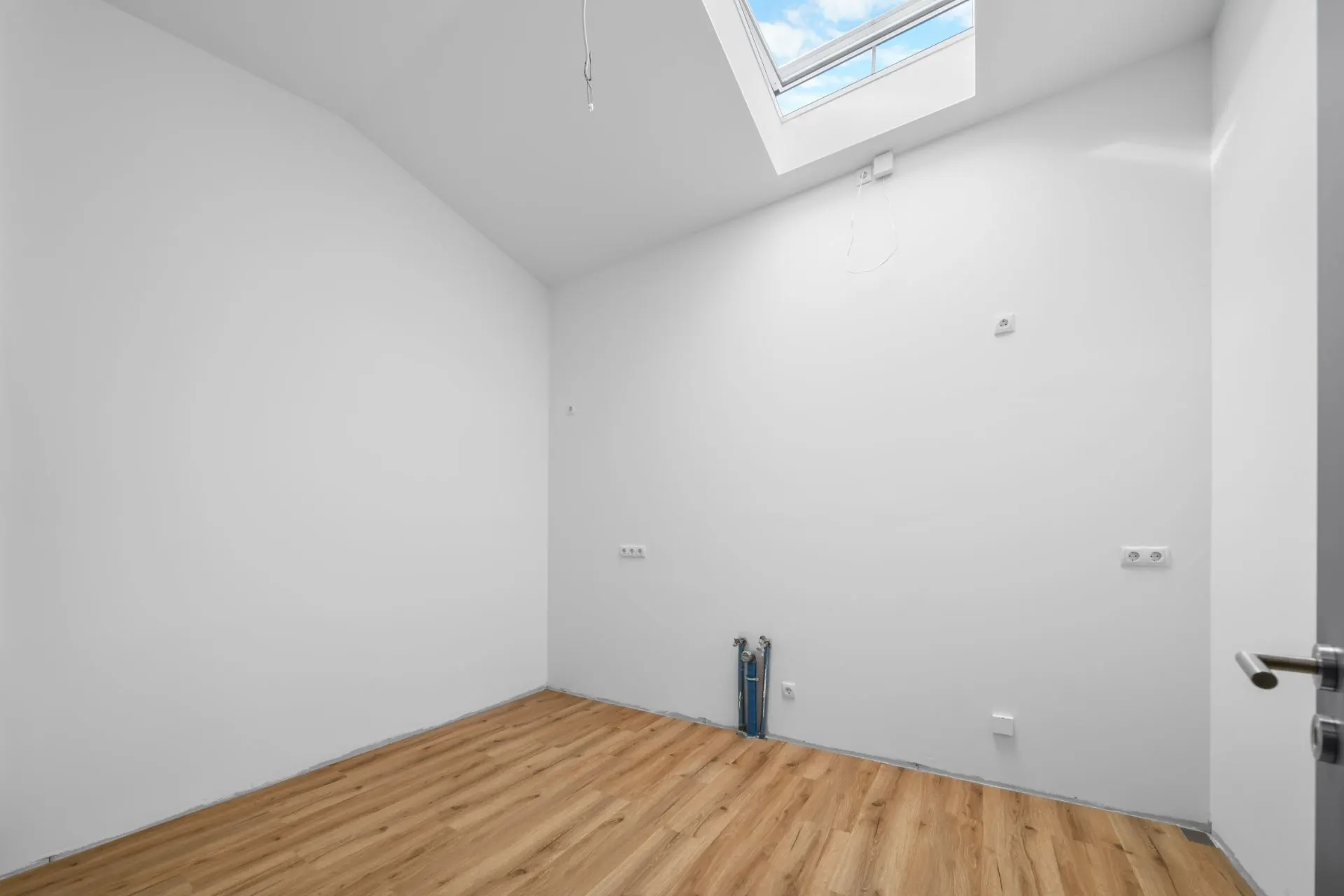 Leerer Raum mit weißer Wand, Holzfußboden und Dachfenster.