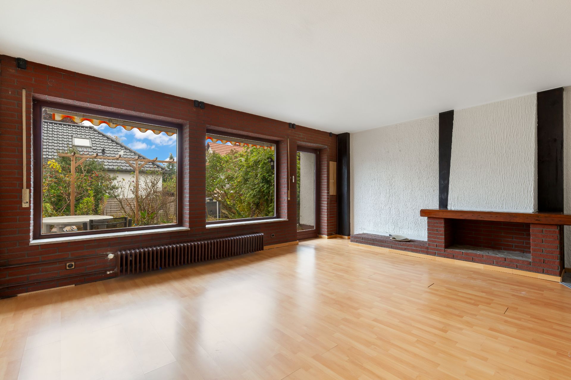 Helles Wohnzimmer mit großen Fenstern, Parkettboden und Kamin, Blick auf Garten.