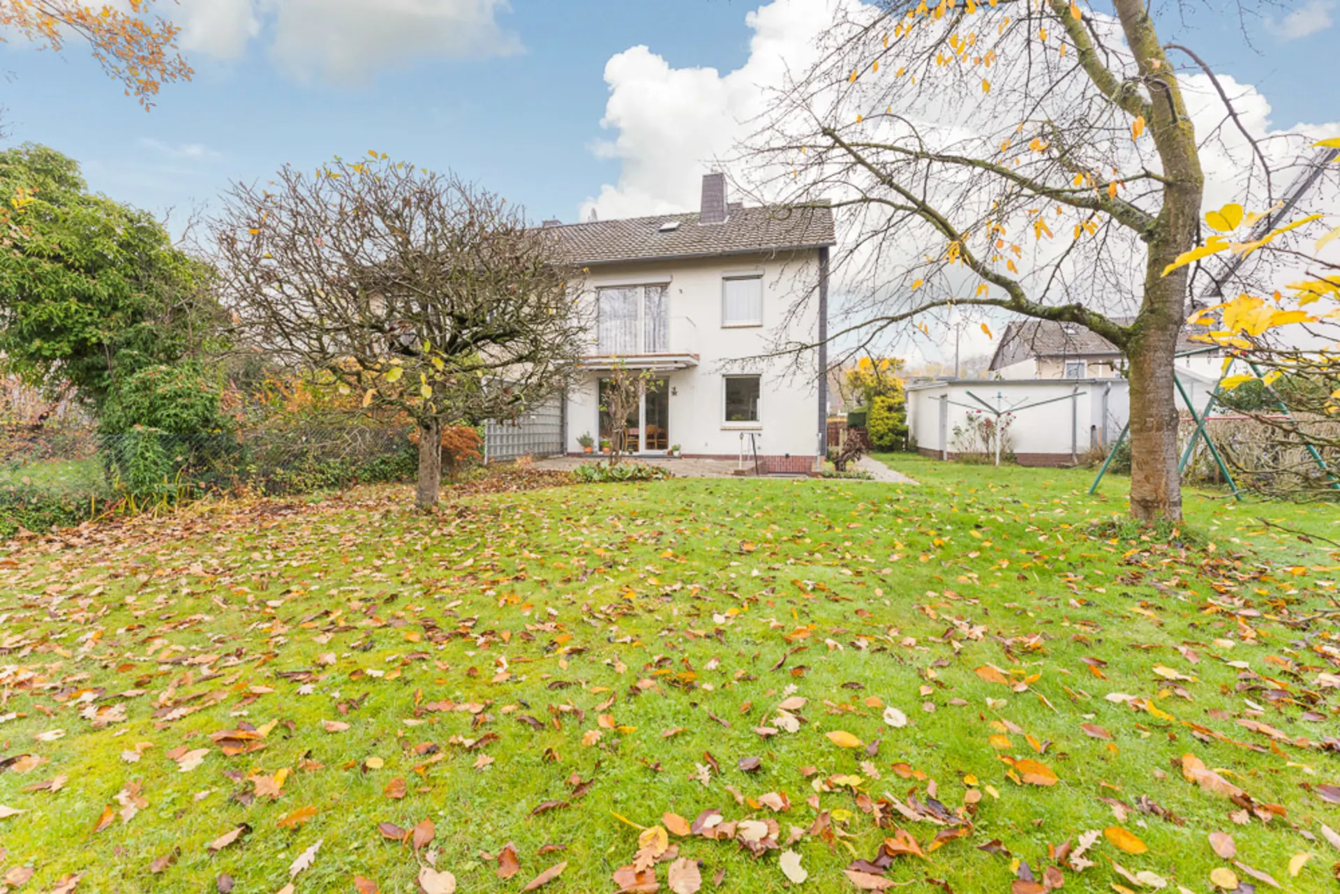 Zweistöckiges Wohnhaus mit großem Garten und herbstlich bedecktem Rasen.