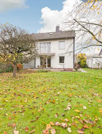 Zweistöckiges Wohnhaus mit großem Garten und herbstlich bedecktem Rasen.