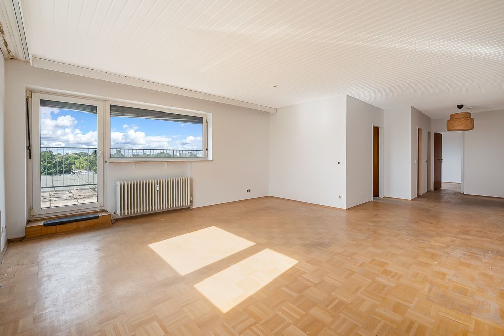 Heller, leerer Wohnraum mit Parkettboden, großen Fenstern und Zugang zu einer Terrasse.