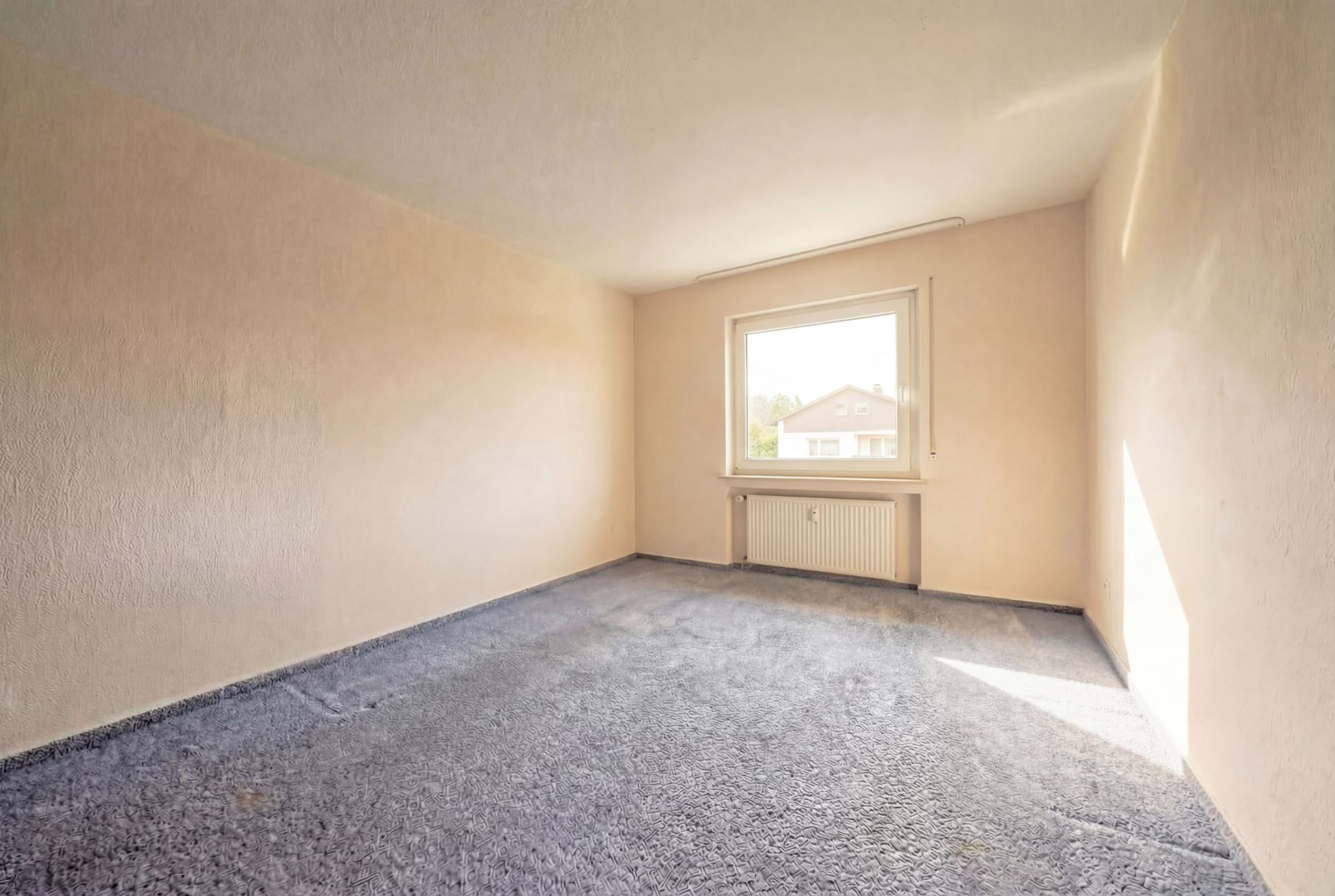 Leerer Raum mit Teppichboden, beigem Wänden und großem Fenster.
