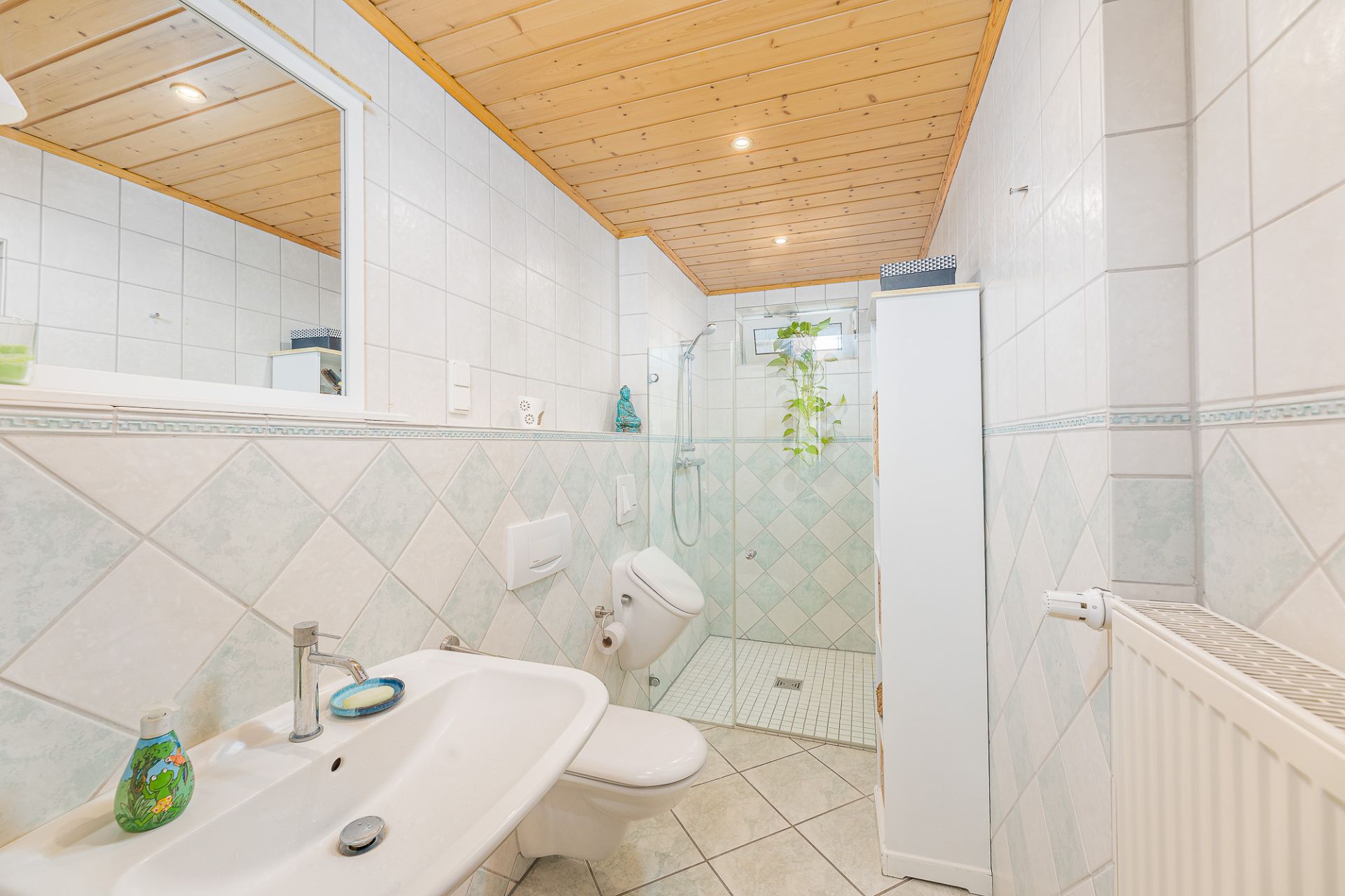 Helles Badezimmer mit Waschbecken, Toilette, bodengleicher Dusche und weißem Fliesenspiegel.