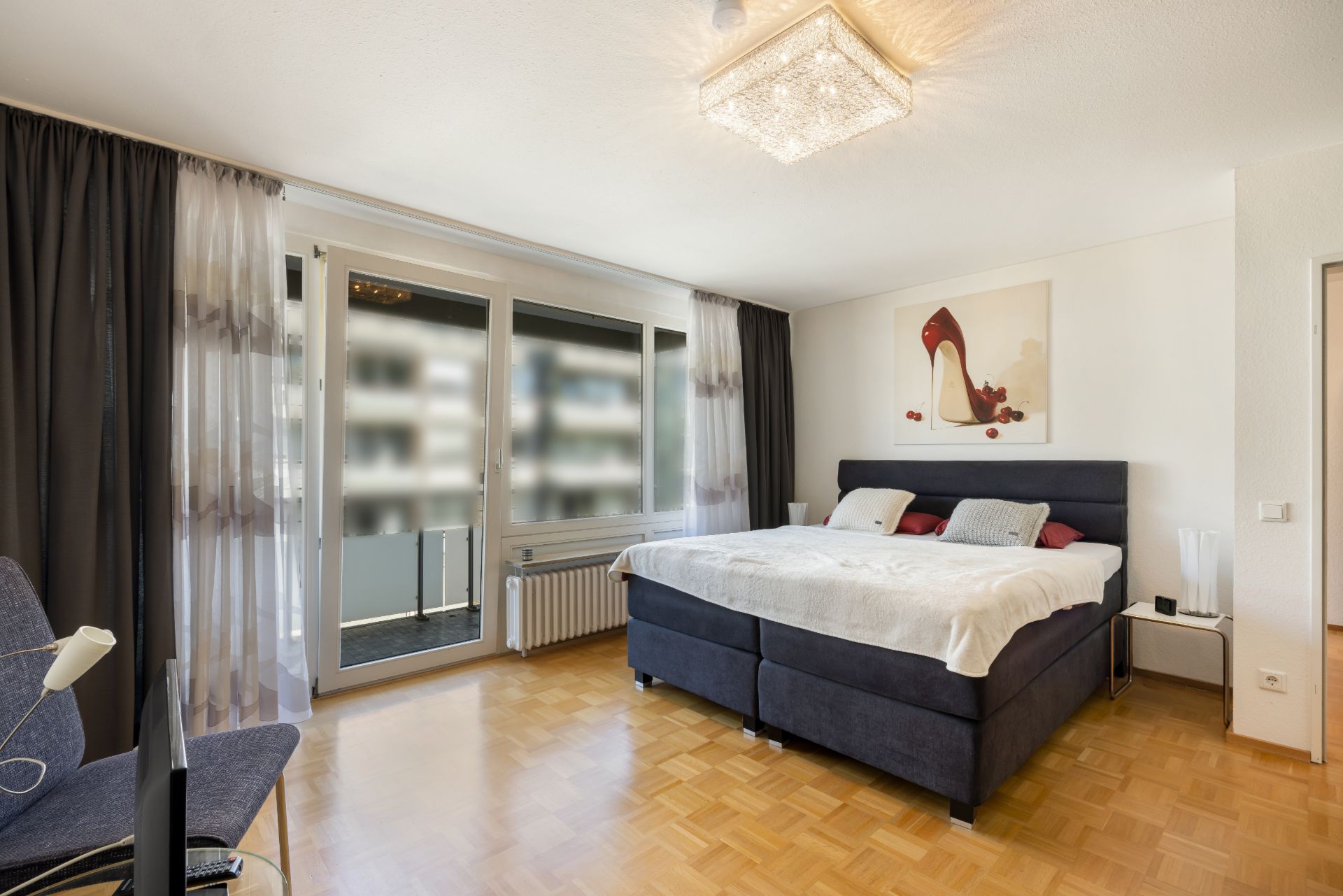 Helles Schlafzimmer mit Doppelbett, Parkettboden, großem Fenster und Balkonzugang.