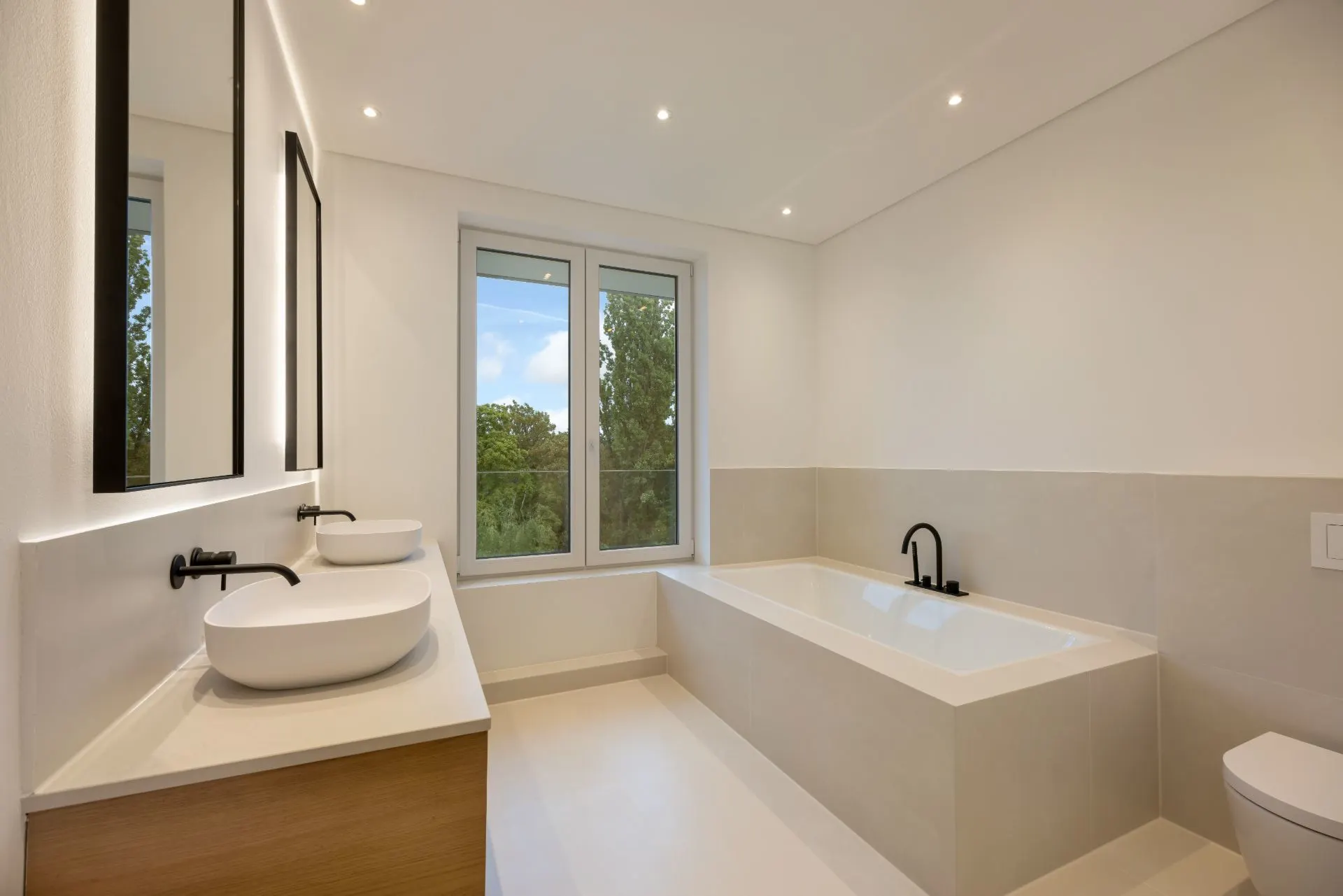 Modernes Badezimmer mit Doppelwaschbecken, Badewanne und Fenster mit Blick ins Grüne.