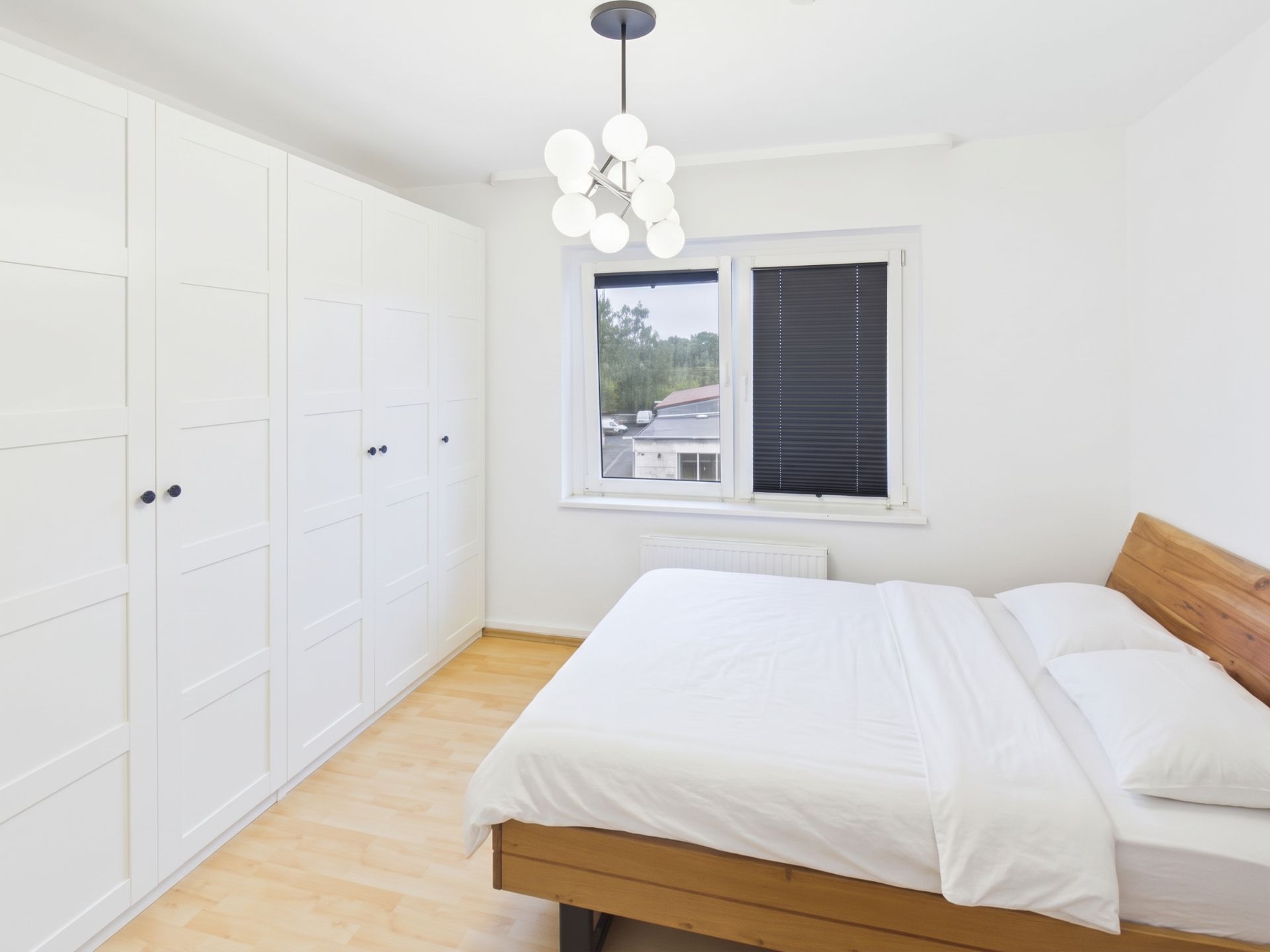 Schlafzimmer mit großem Bett, weißen Kleiderschränken und Fenster mit Jalousien.