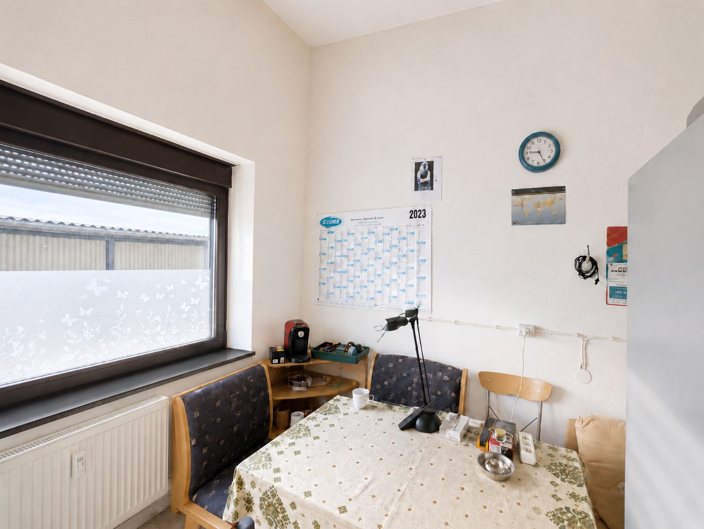 Kleiner Essbereich mit Tisch, Stühlen, Eckbank, Uhr, Kalender und Fenster.