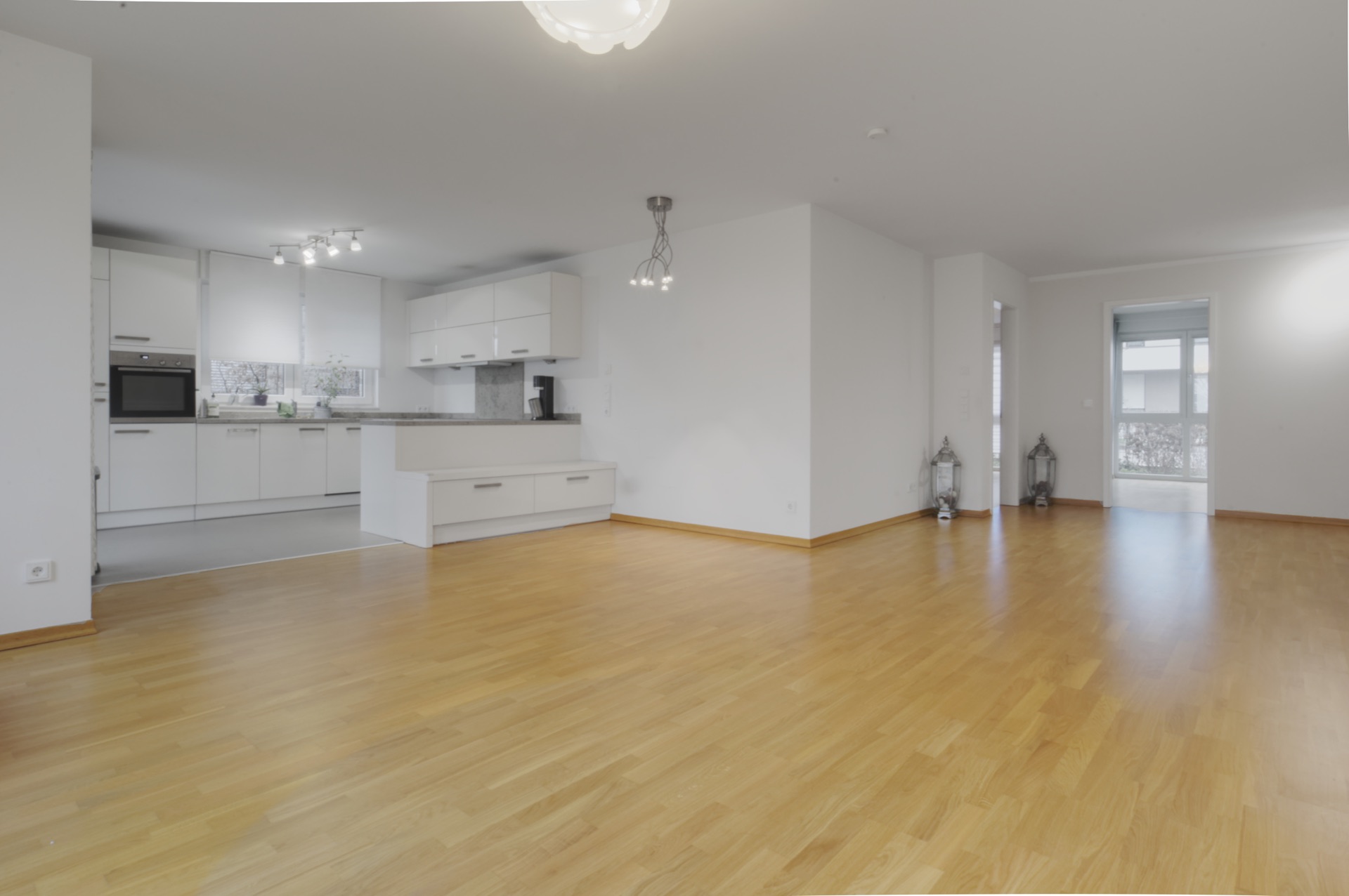 Helles Wohnzimmer mit Parkettboden und offener, moderner Küche im Hintergrund.