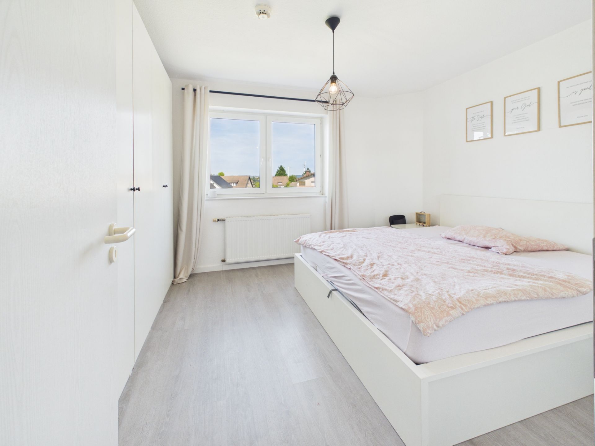 Helles Schlafzimmer mit Doppelbett, großem Fenster, weißem Schrank und hellem Boden.