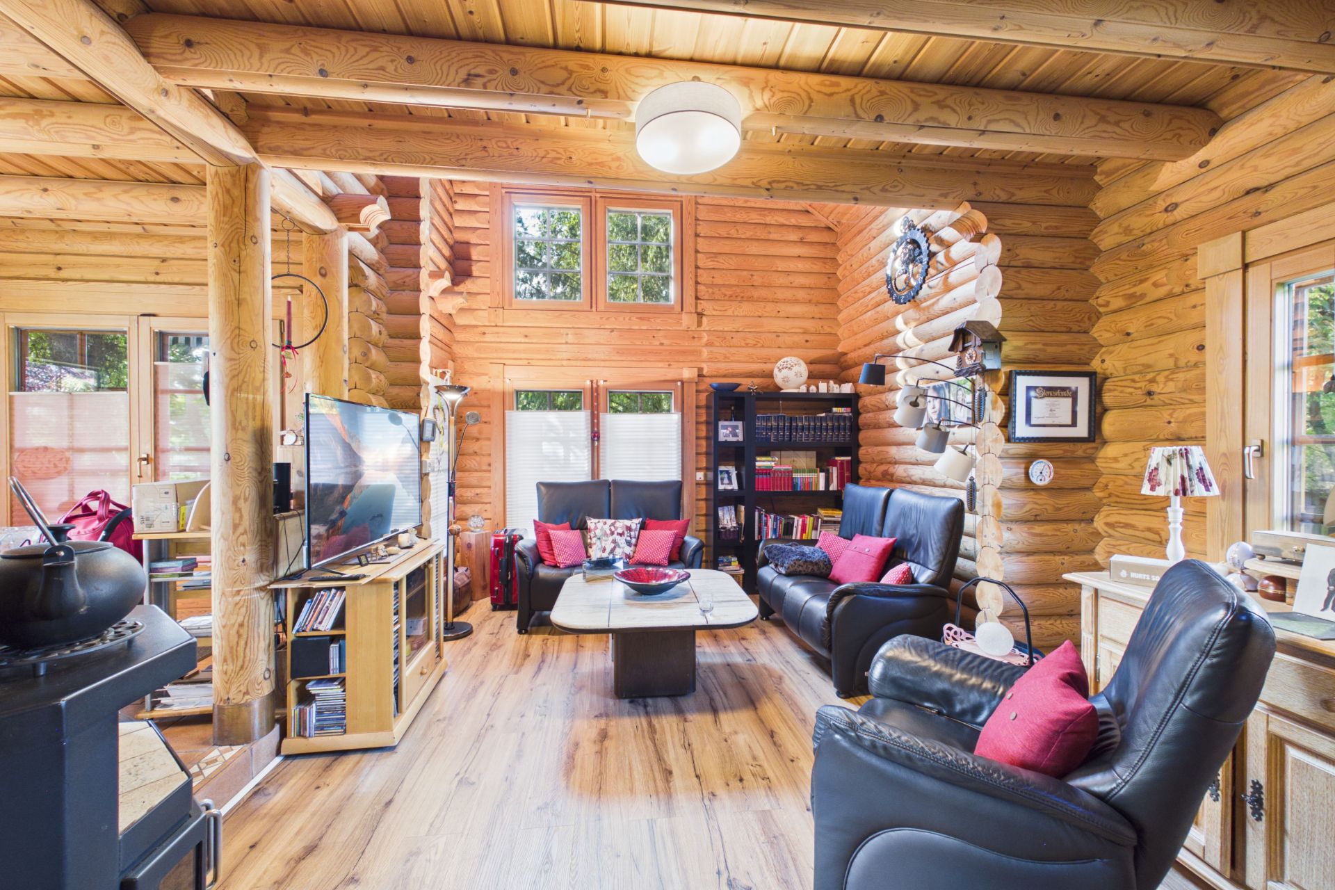 Gemütliches Wohnzimmer aus Holz mit Sofa, Sesseln, Fernseher und großen Fenstern.