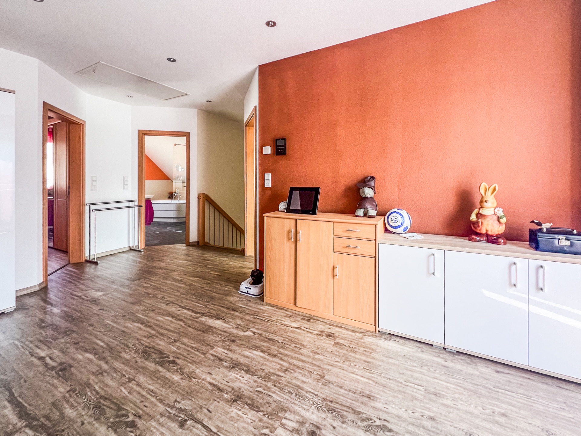 Heller Flur mit Holzboden, orangener Wand und Sideboard mit Dekorationen.