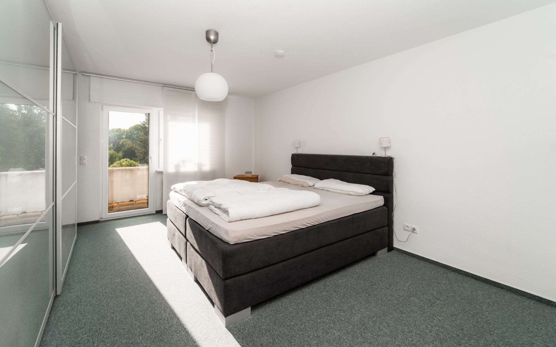 Helles Schlafzimmer mit großem Bett, Kleiderschrank und Zugang zu einem Balkon.