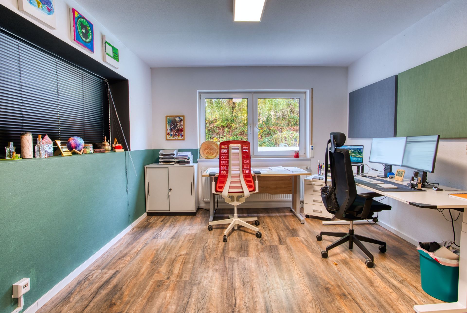 Modernes Homeoffice mit zwei Schreibtischen, Bürostühlen und großen Monitoren, Holzfußboden und Fenster.