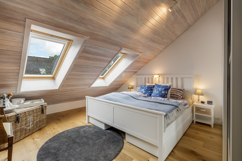 Helles Schlafzimmer mit Dachschräge, Doppelbett, zwei Dachfenstern und Holzboden.