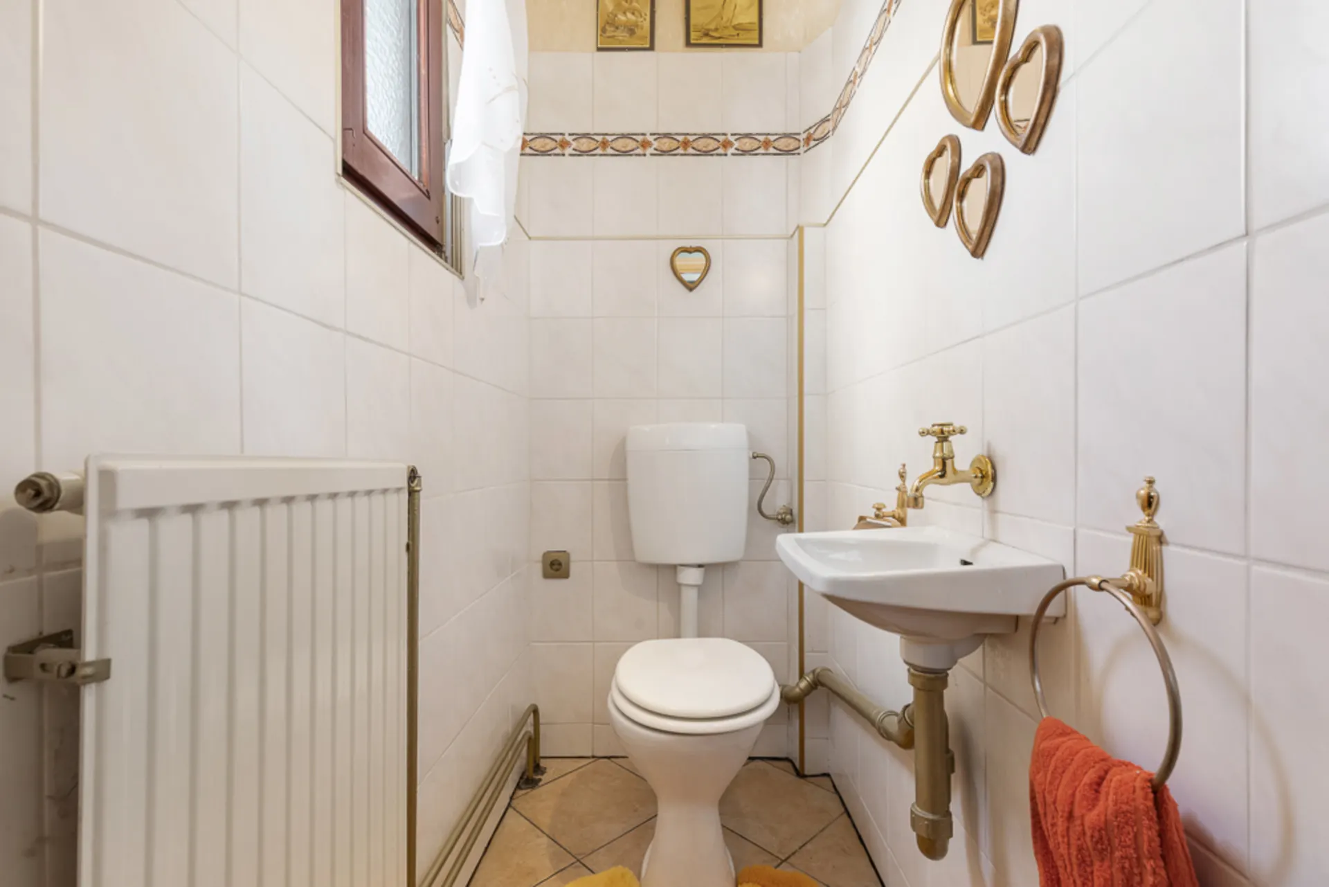 Kleines Badezimmer mit Toilette, Waschbecken, Heizkörper und Spiegeln an der Wand.