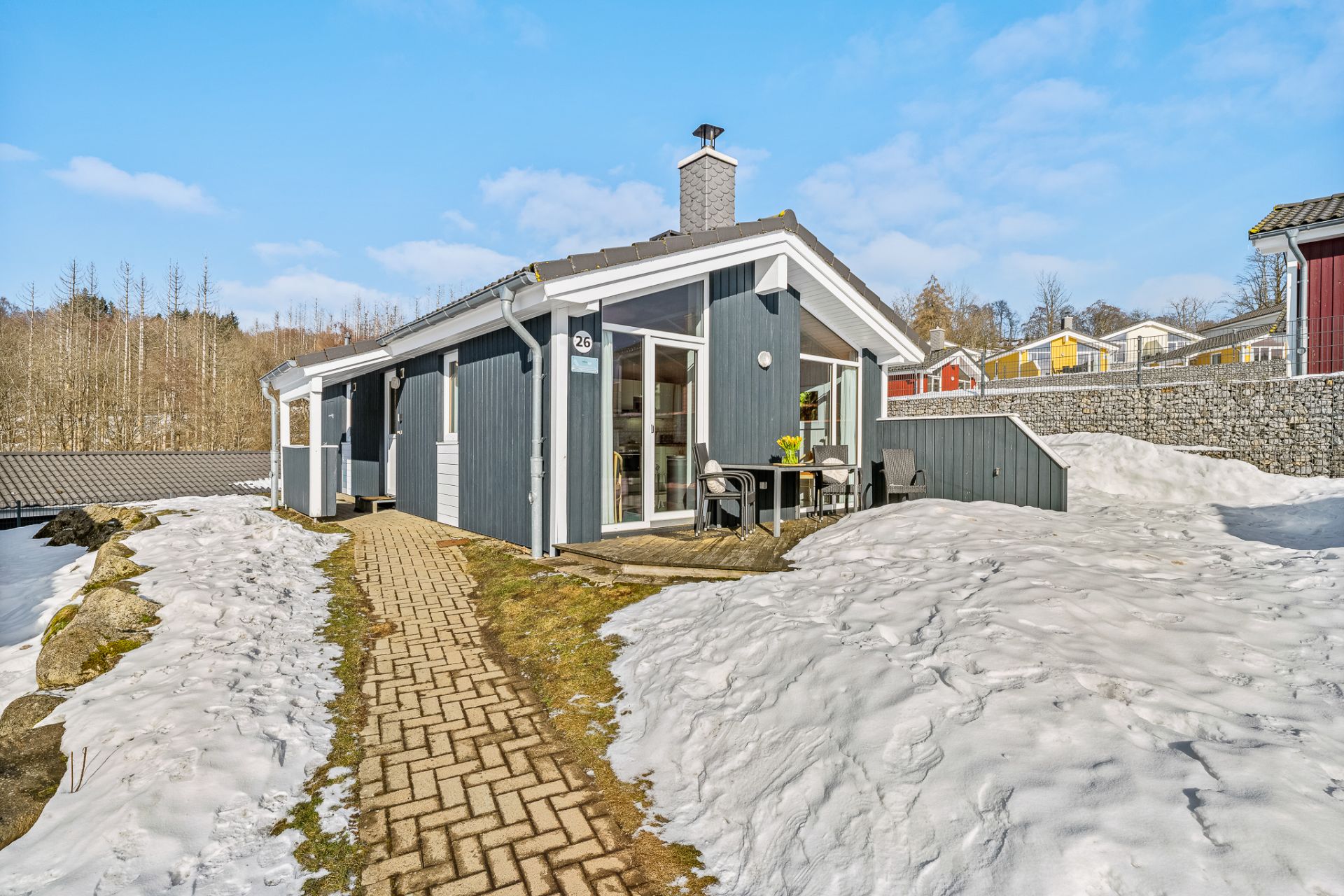Modernes graues Haus mit Terrasse, gepflastertem Weg und Schnee im Garten.