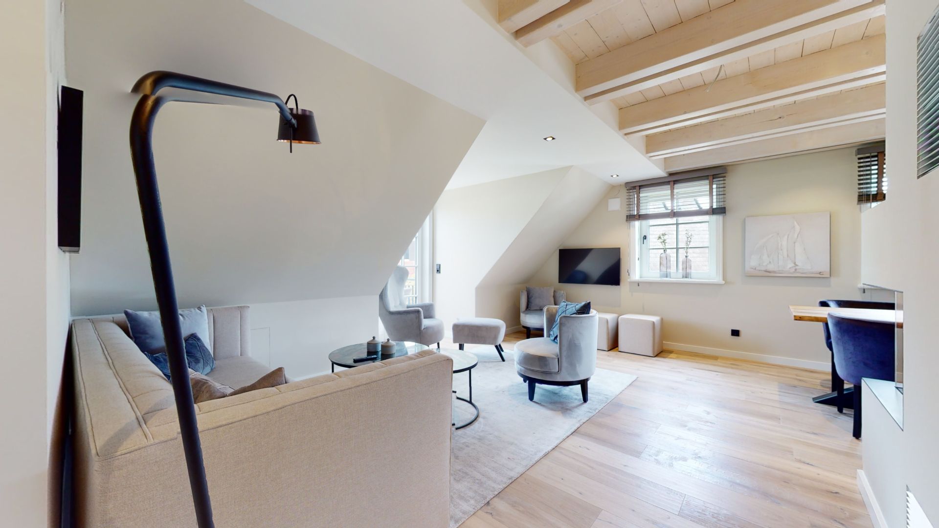 Helles Wohnzimmer mit Couch, Sesseln, Fernseher und Holzboden unter Dachschrägen.