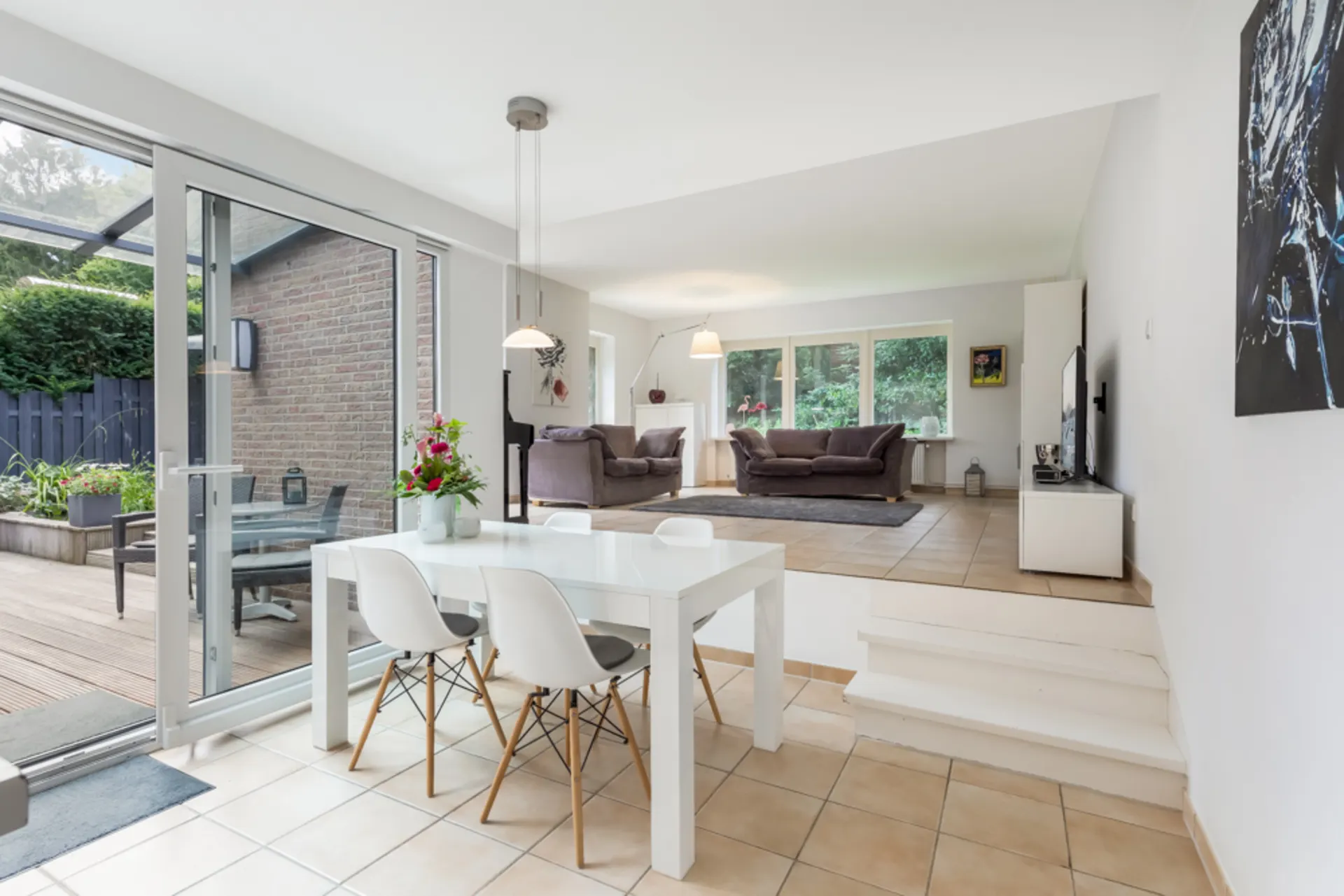 Helles Wohnzimmer mit Essbereich, Tisch mit Stühlen und Zugang zur Terrasse, Sofa und Fernseher.
