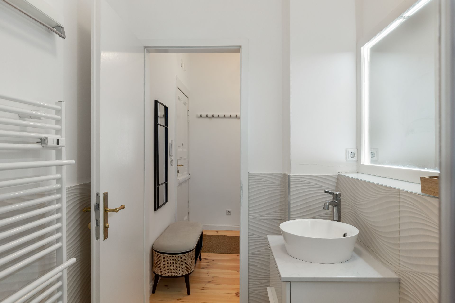 Modernes Bad mit rundem Waschbecken, Spiegel, Handtuchwärmer und Blick in den Flur mit Bank.