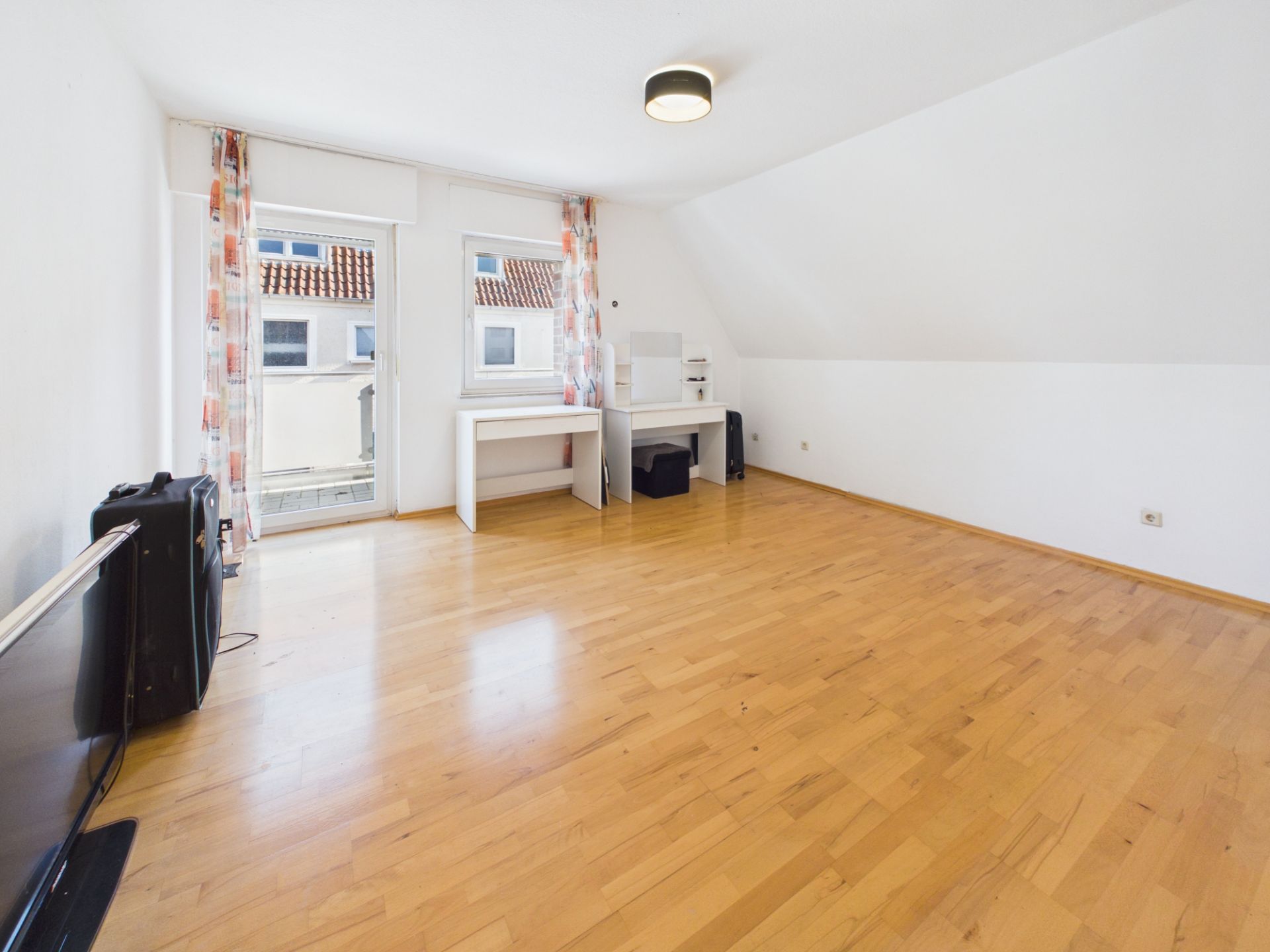 Helles Zimmer mit Holzfußboden, Schreibtischen, Fenstern und einer Glastür mit Vorhängen.