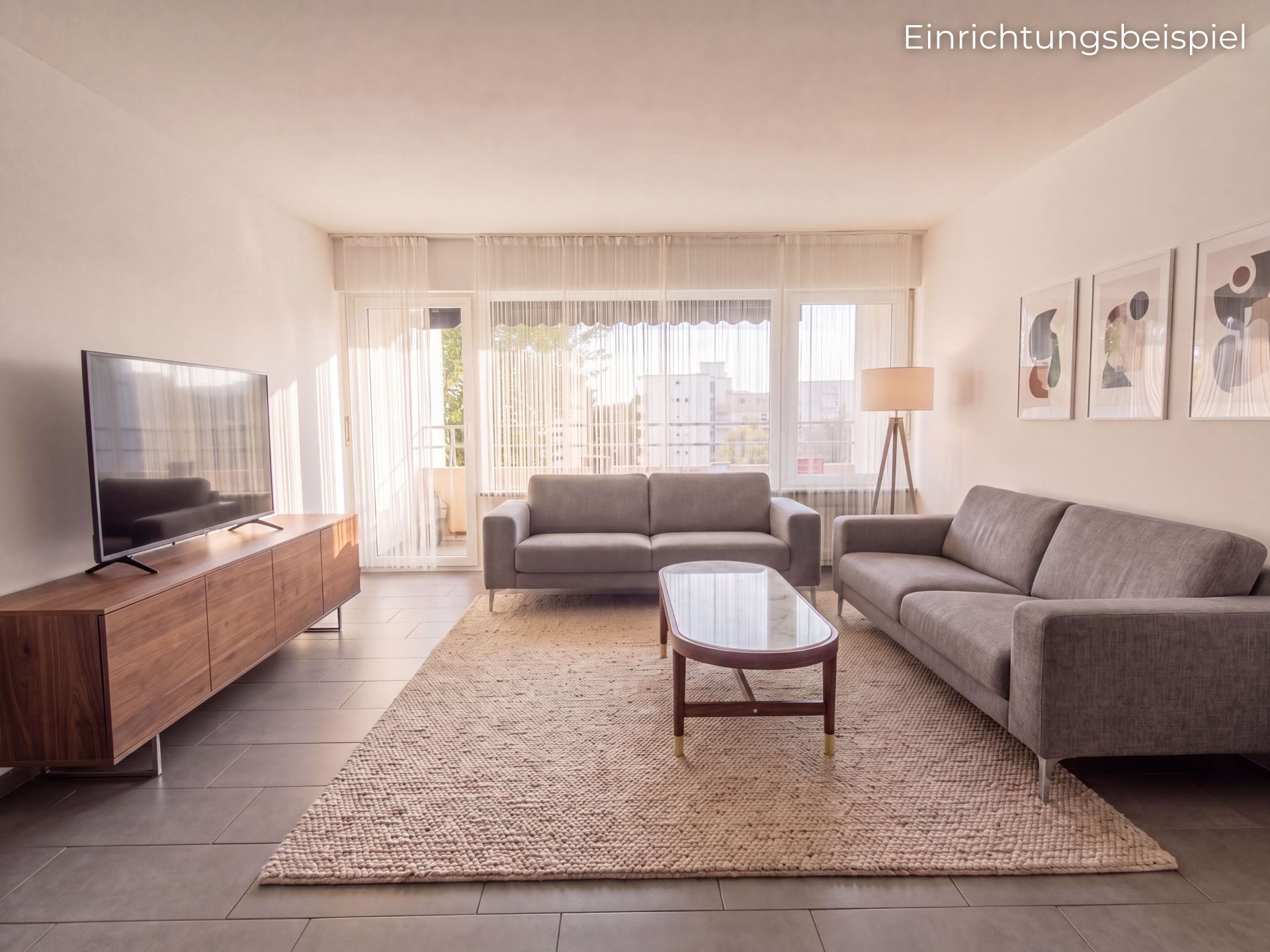 Helles Wohnzimmer mit zwei grauen Sofas, Couchtisch, Teppich, TV und Stehlampe vor großen Fenstern.