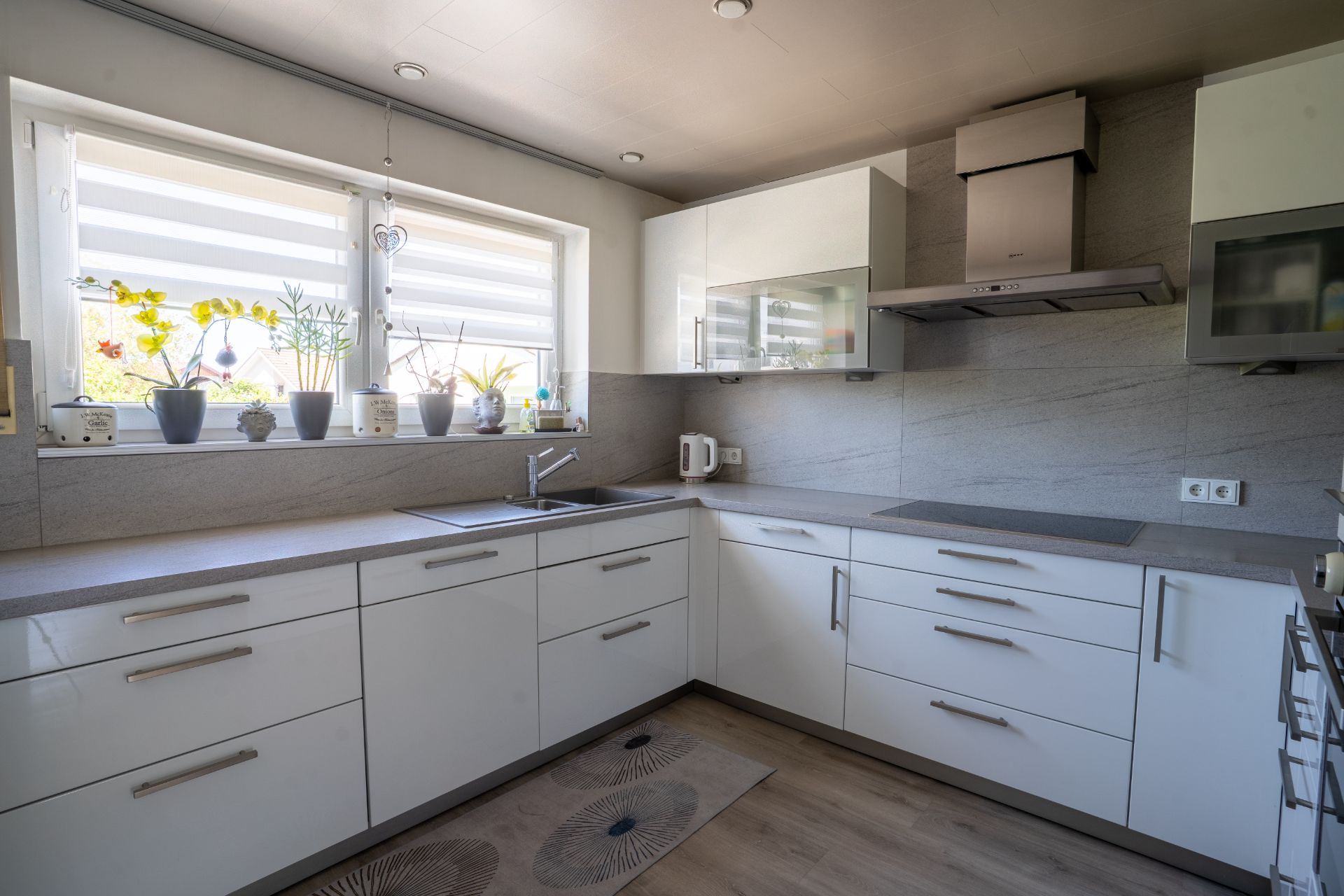 Moderne weiße Einbauküche mit vielen Schubladen und Pflanzen auf der Fensterbank.