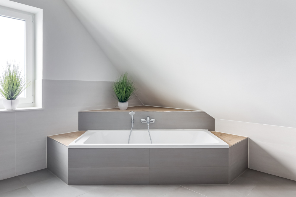 Modernes Badezimmer mit Badewanne unter einer Schräge und drei grünen Pflanzen in Töpfen.