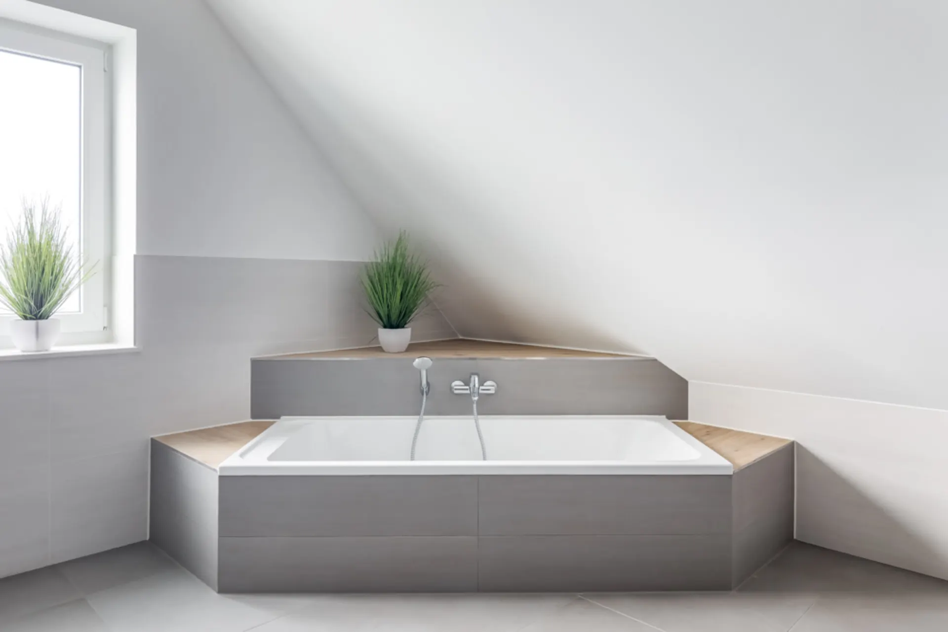 Modernes Badezimmer mit Badewanne unter einer Schräge und drei grünen Pflanzen in Töpfen.