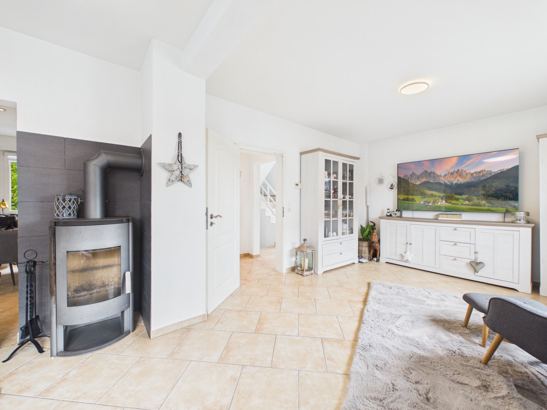 Helles Wohnzimmer mit Kamin, Teppich, Schrank, Fernseher und Kommode auf Fliesenboden.