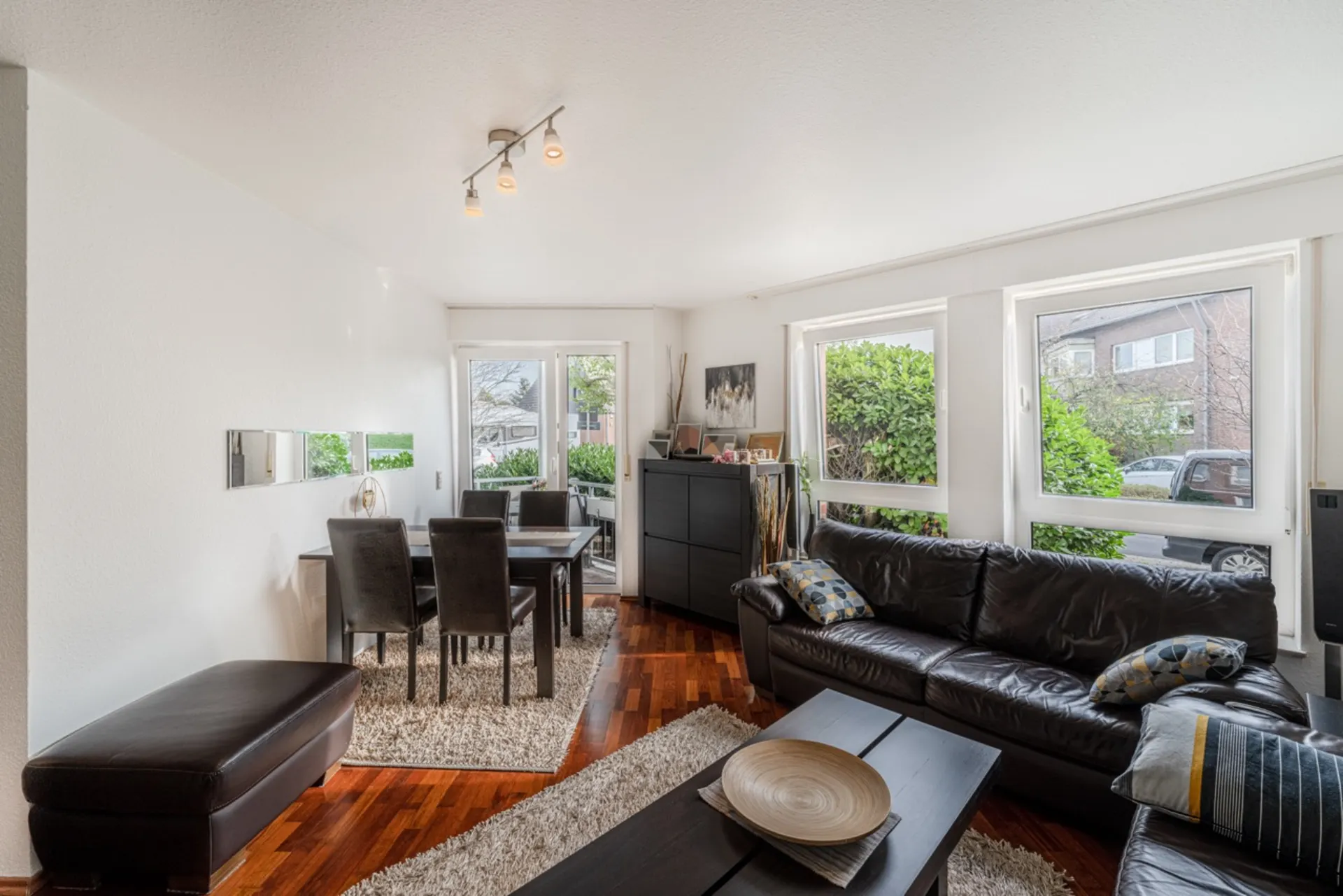 Wohnzimmer mit braunen Ledersofas, Esstisch, großen Fenstern und Holzboden.