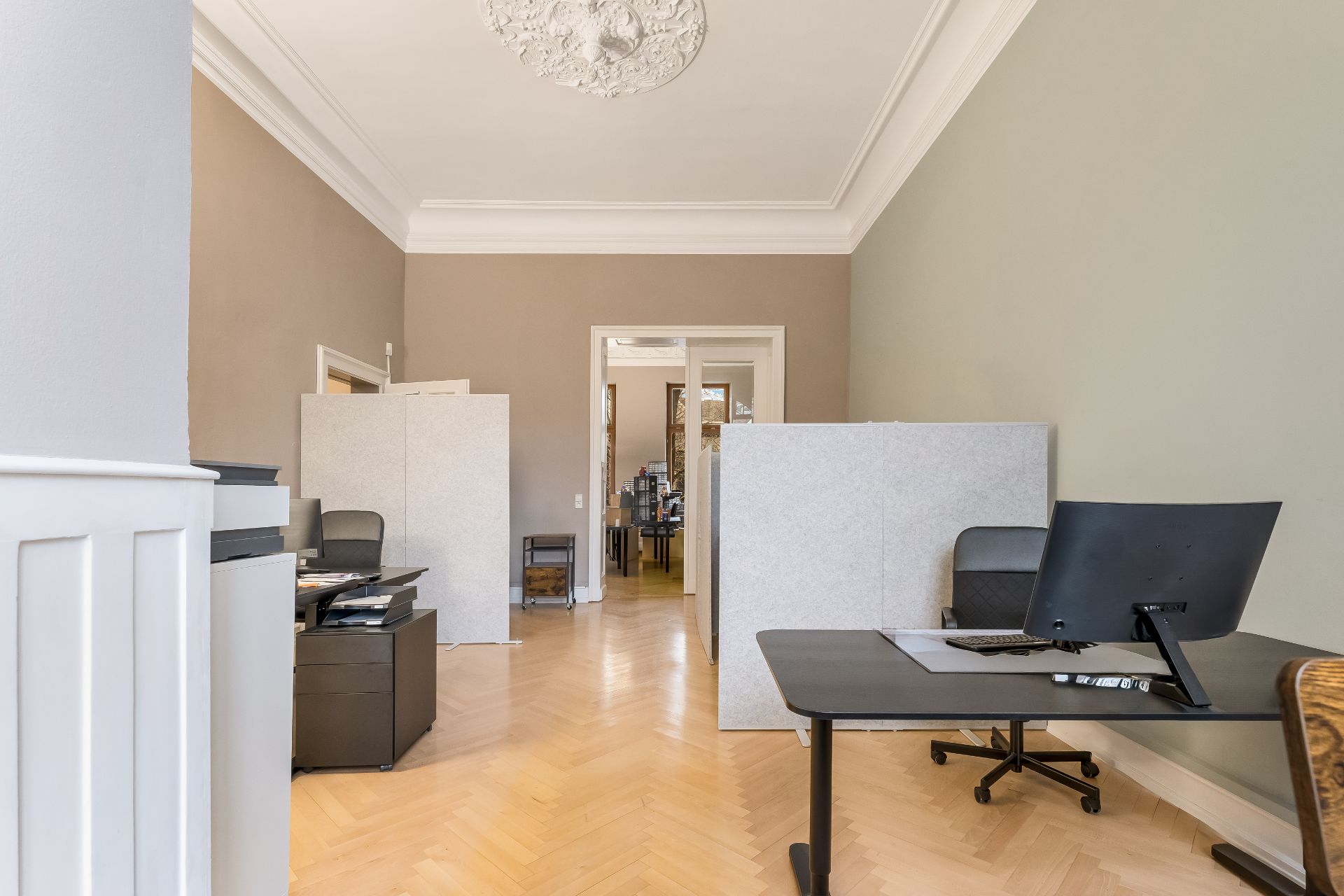 Helles Zimmer mit Holzboden, Schreibtischen, Stühlen und Raumteilern.