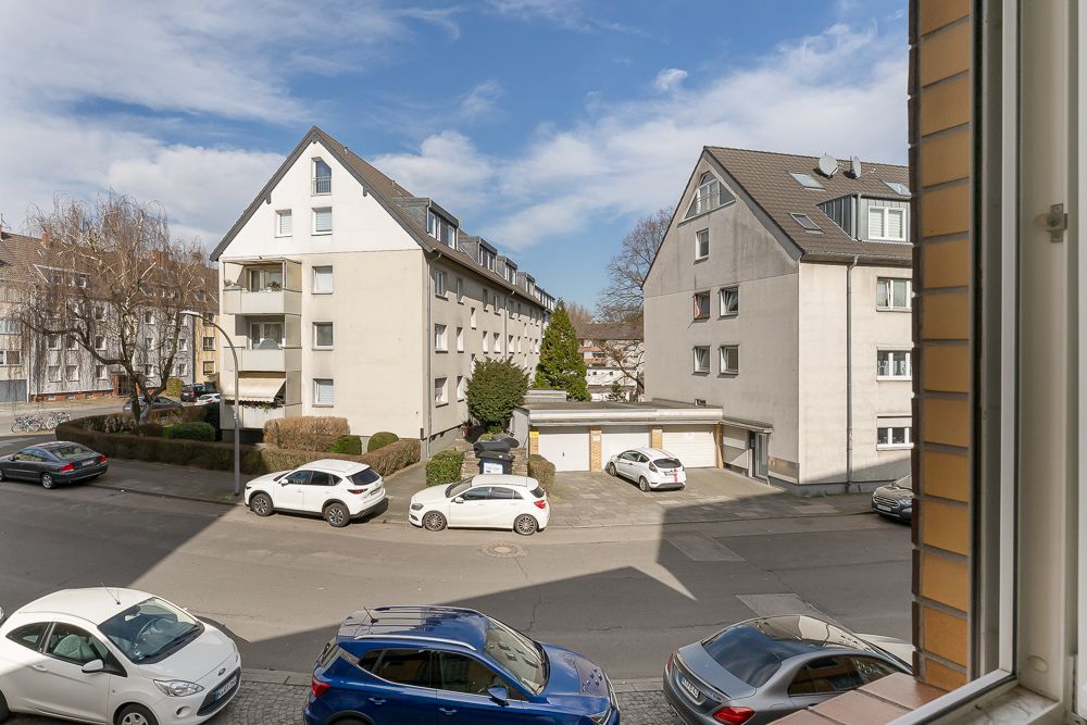 Blick aus dem Fenster auf Wohngebäude, geparkte Autos und Straße bei Tageslicht.