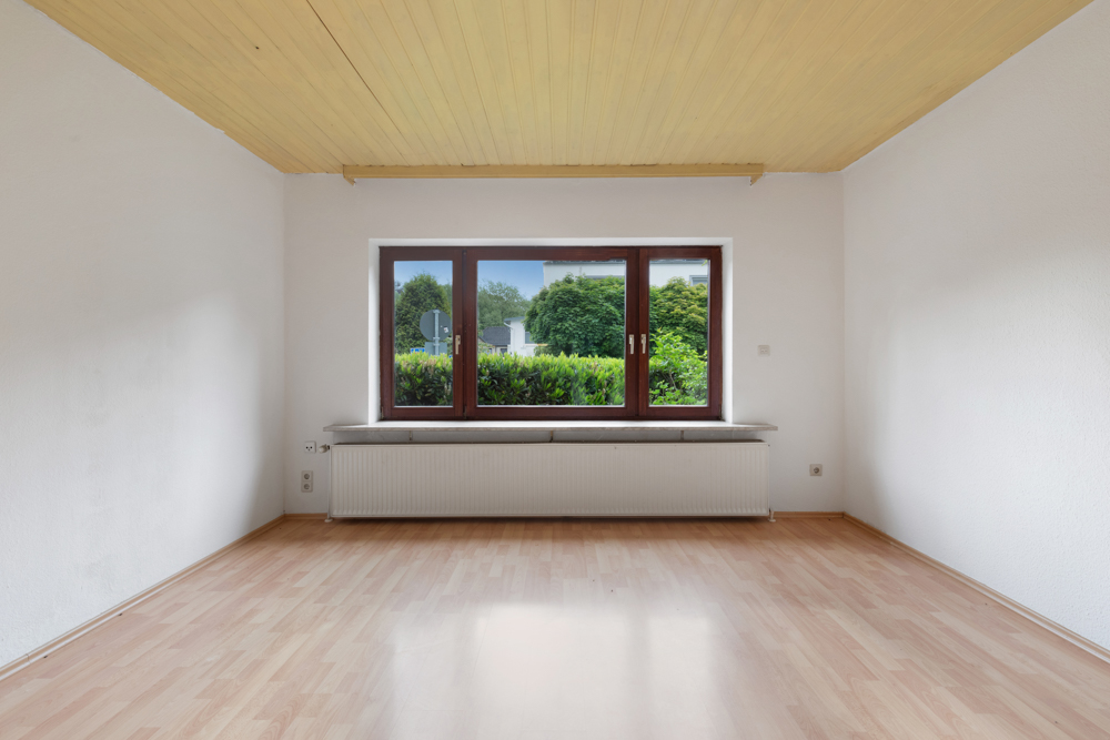 Leerer Raum mit Holzdecke, Laminatboden und großem Fenster mit Blick auf Garten.