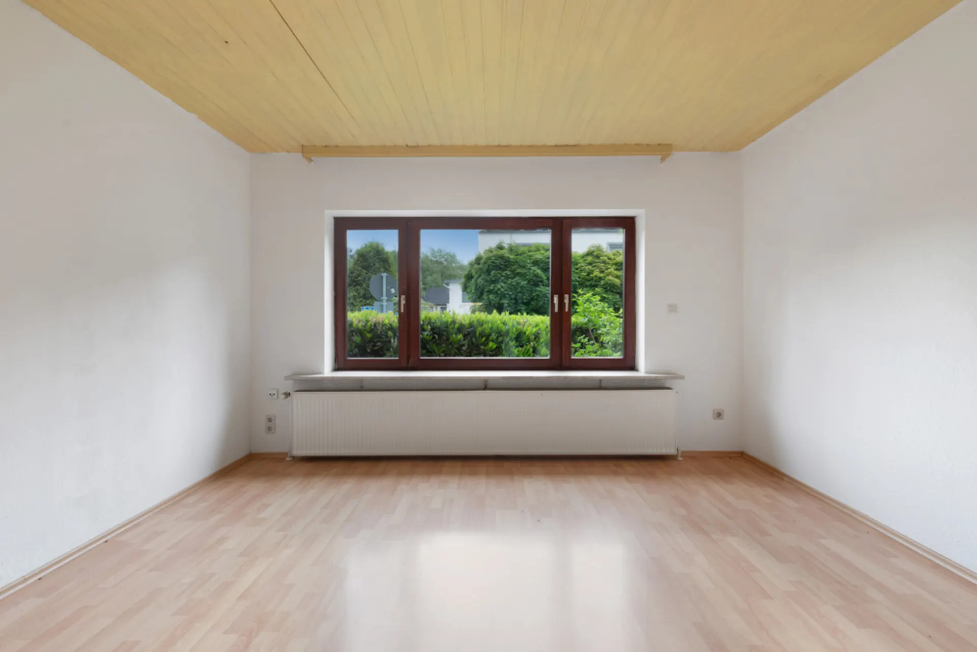 Leerer Raum mit Holzdecke, Laminatboden und großem Fenster mit Blick auf Garten.