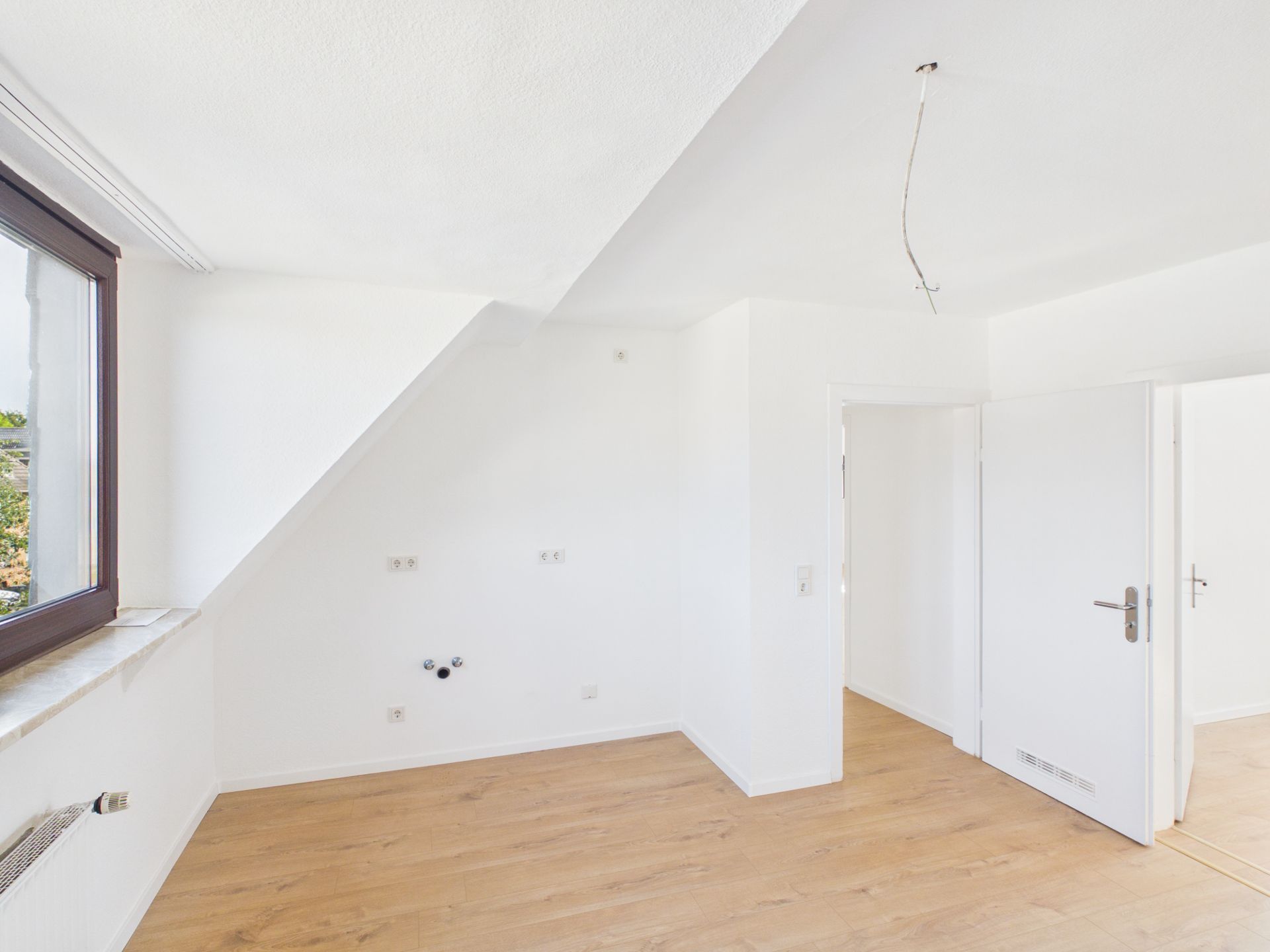 Heller, leerer Raum mit weißer Wand, Holzfußboden und großem Fenster.