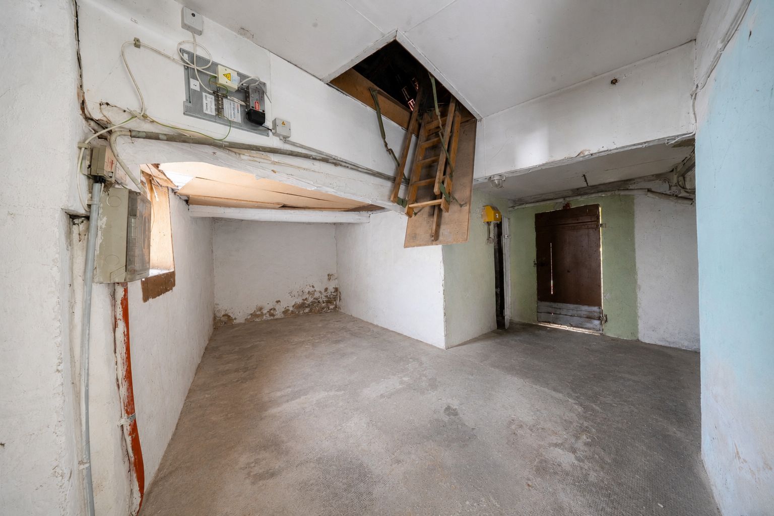 Kleiner Kellerraum mit offenem Fenster, Leiter zur Decke und brauner Tür.