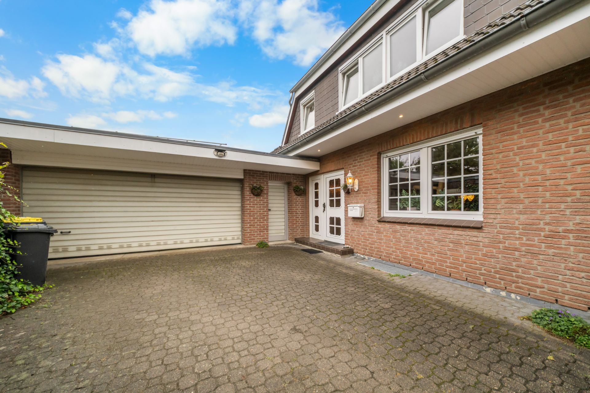 Einfahrt mit Pflastersteinen, Garage mit Rolltor und Hauseingang an einem Wohnhaus.