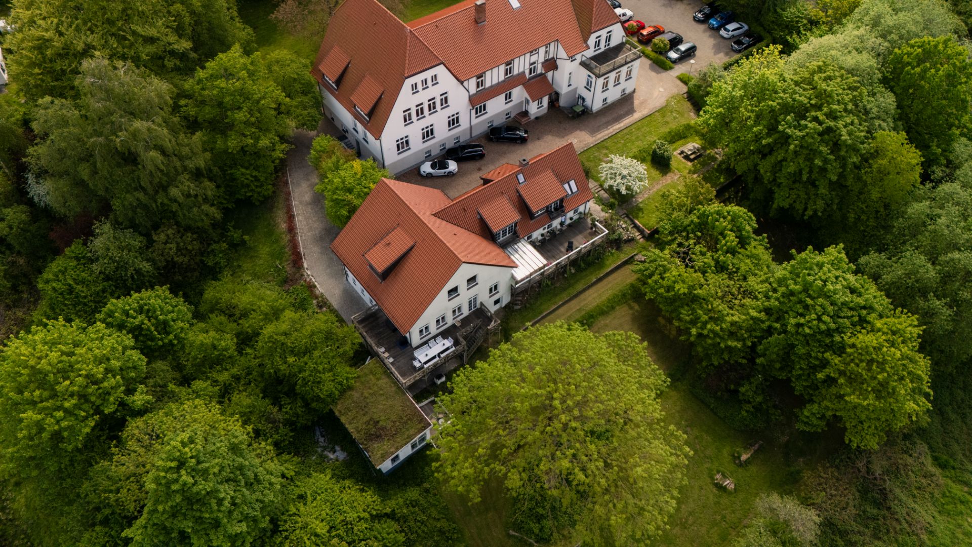 Luftaufnahme eines großen Wohnhauses mit roten Dächern, umgeben von vielen grünen Bäumen.