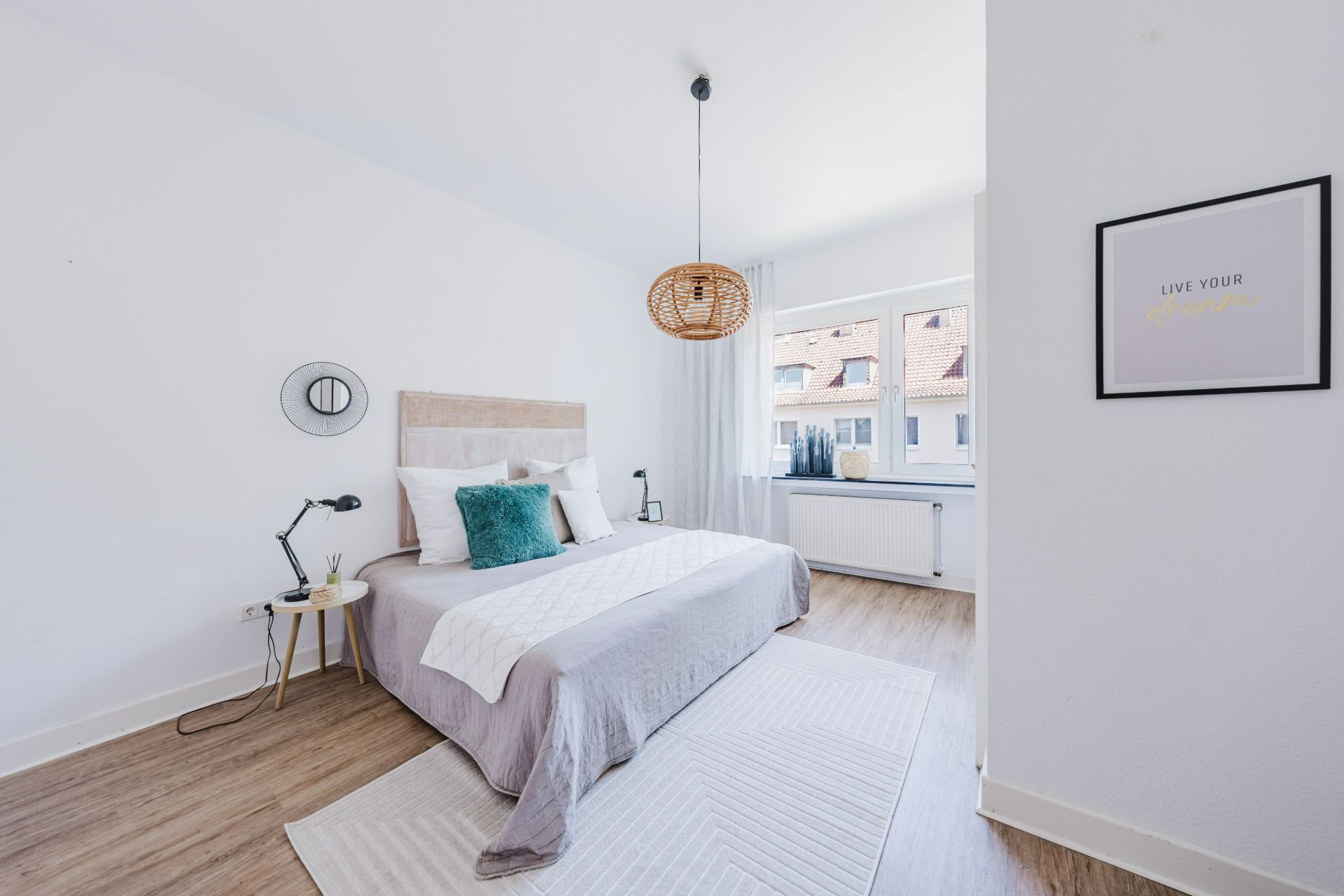 Helles Schlafzimmer mit Doppelbett, Nachttischen, Holzlaminat und großem Fenster.