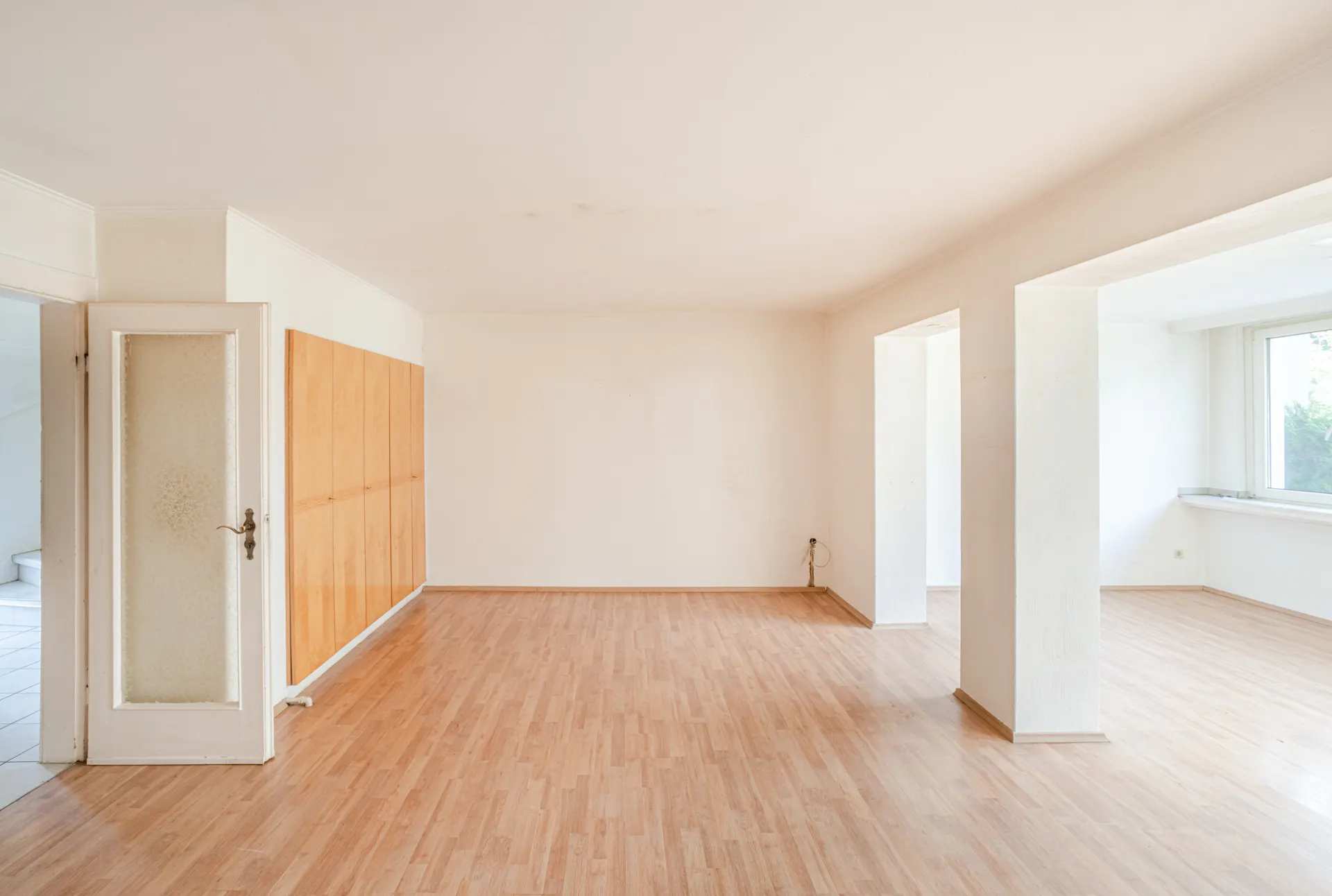 Helles, leeres Wohnzimmer mit Holzboden, weißen Wänden und großen Fenstern.