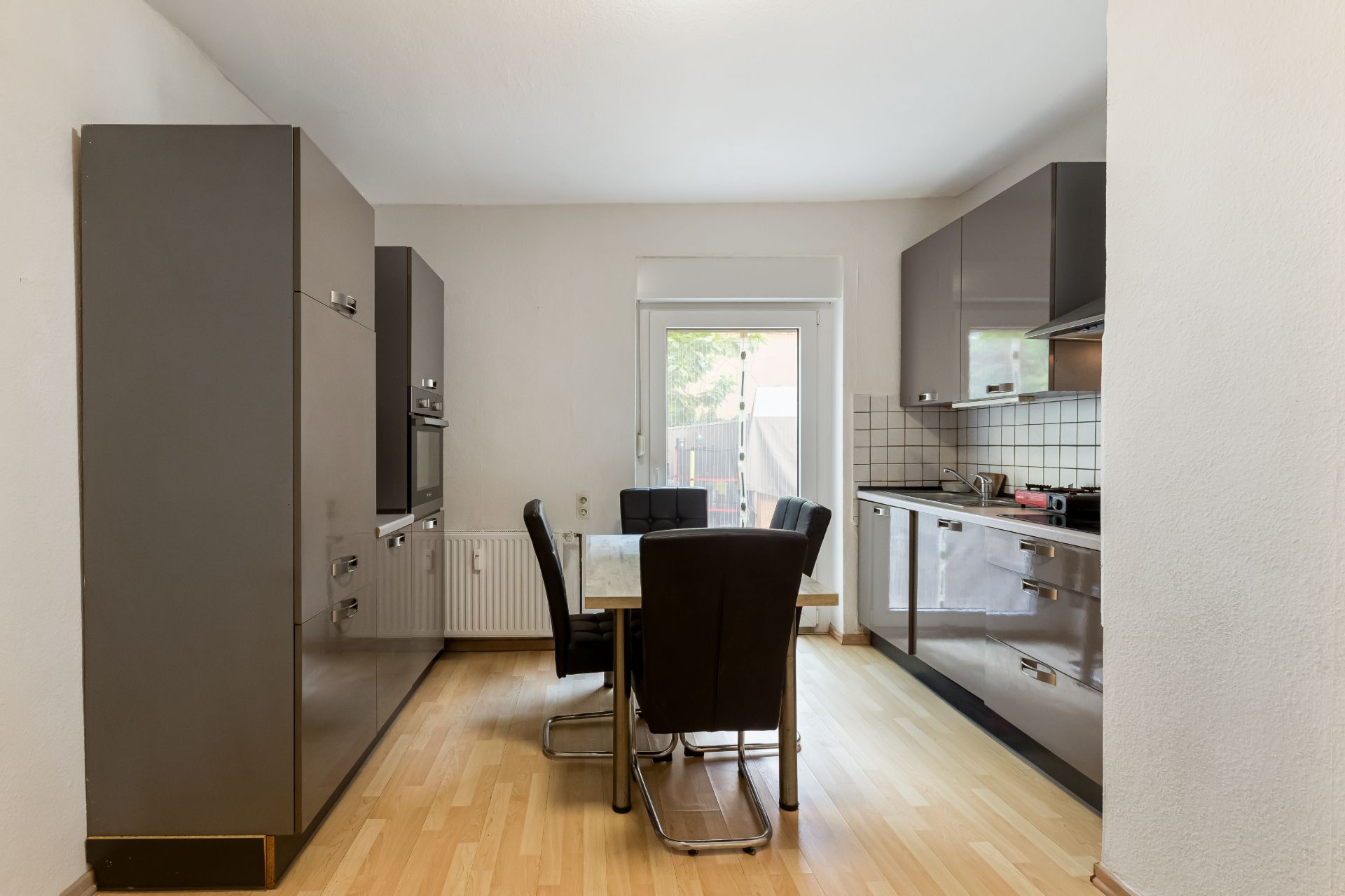 Moderne Küche mit Esstisch, vier Stühlen und großen grauen Schränken, helles Holzfußboden.