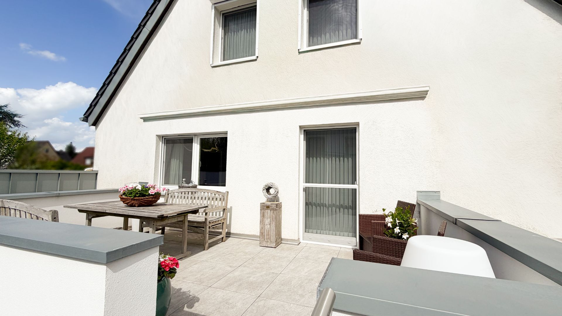 Große Terrasse mit Sitzgruppe und Pflanzen vor einem weißen Wohnhaus.