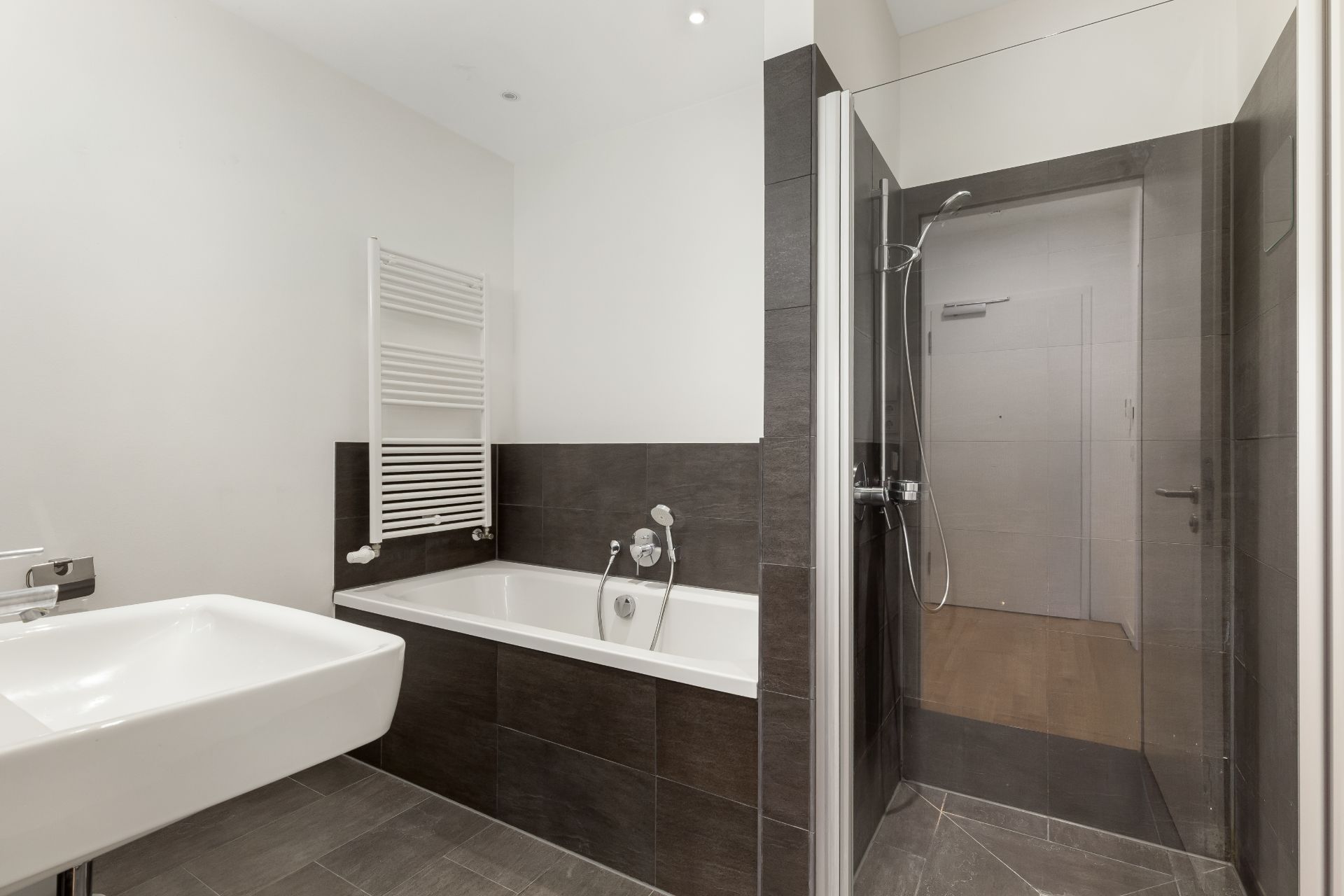 Modernes Badezimmer mit weißem Waschbecken, Badewanne, Dusche und Handtuchheizkörper.